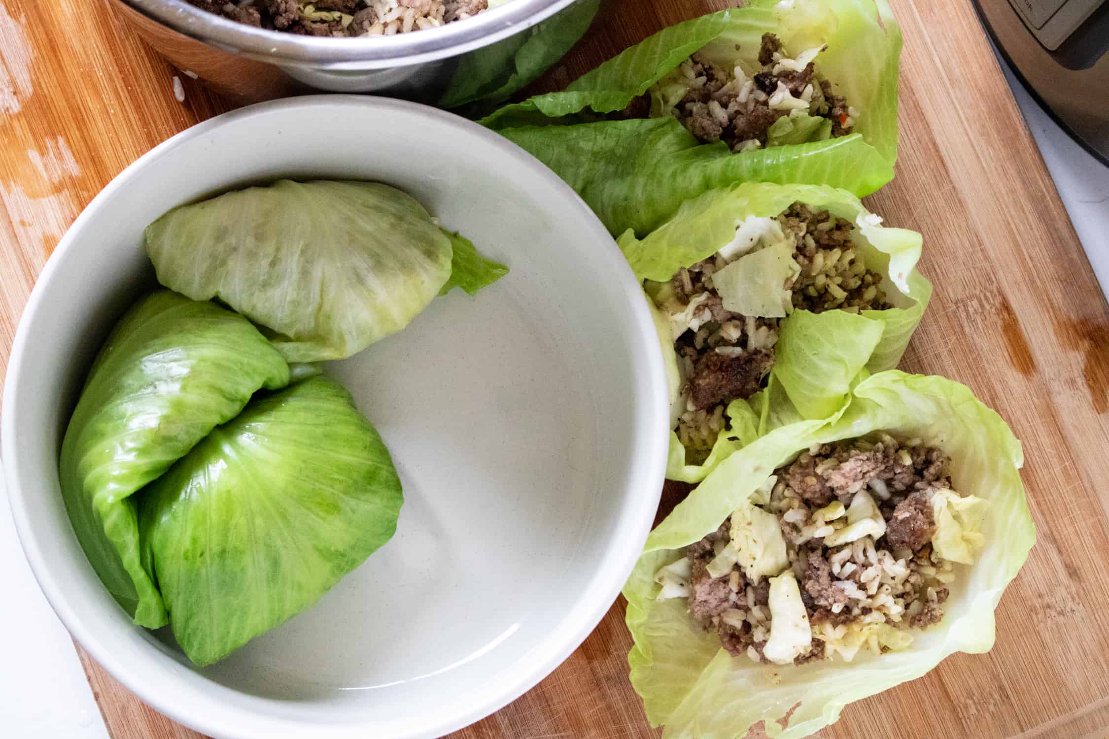 stuffed cabbage leaves being rolled up and placed in a white bowl 