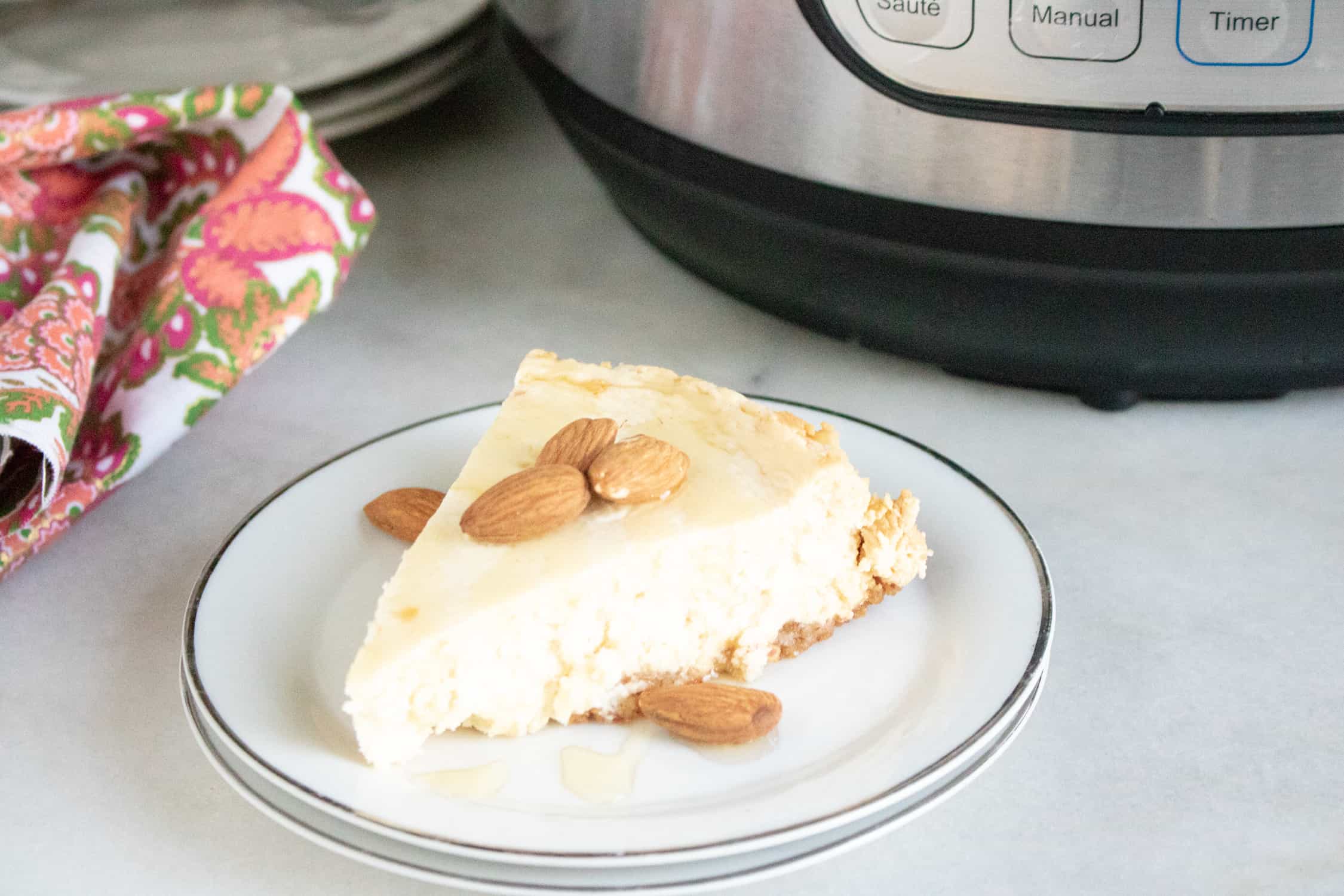Close-up view of a slice of Instant Pot Grain-free Keto Cheesecake served on a white dessert plate and garnished with almonds