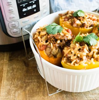 Completed Instant Po Orzo & Italian Sausage Stuffed Peppers in a white ceramic dish in front of the Instant Pot