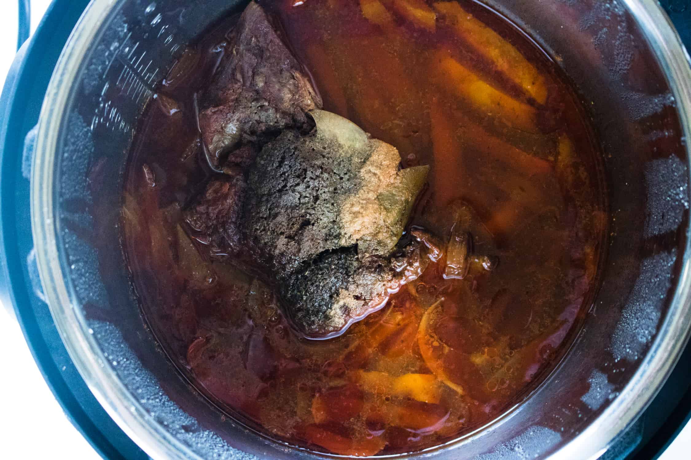 A beef roast and ingredients for Instant Pot Beef Carnitas being cooked inside an Instant Pot