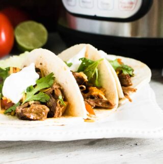 Three soft tacos made with Instant Pot Beef Carnitas served on a white plate
