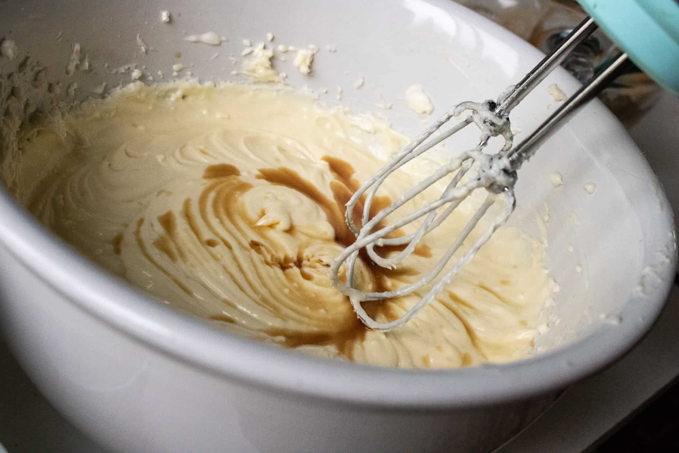vanilla extract being blended into the Instant Pot cheesecake recipe mixture in a white mixing bowl