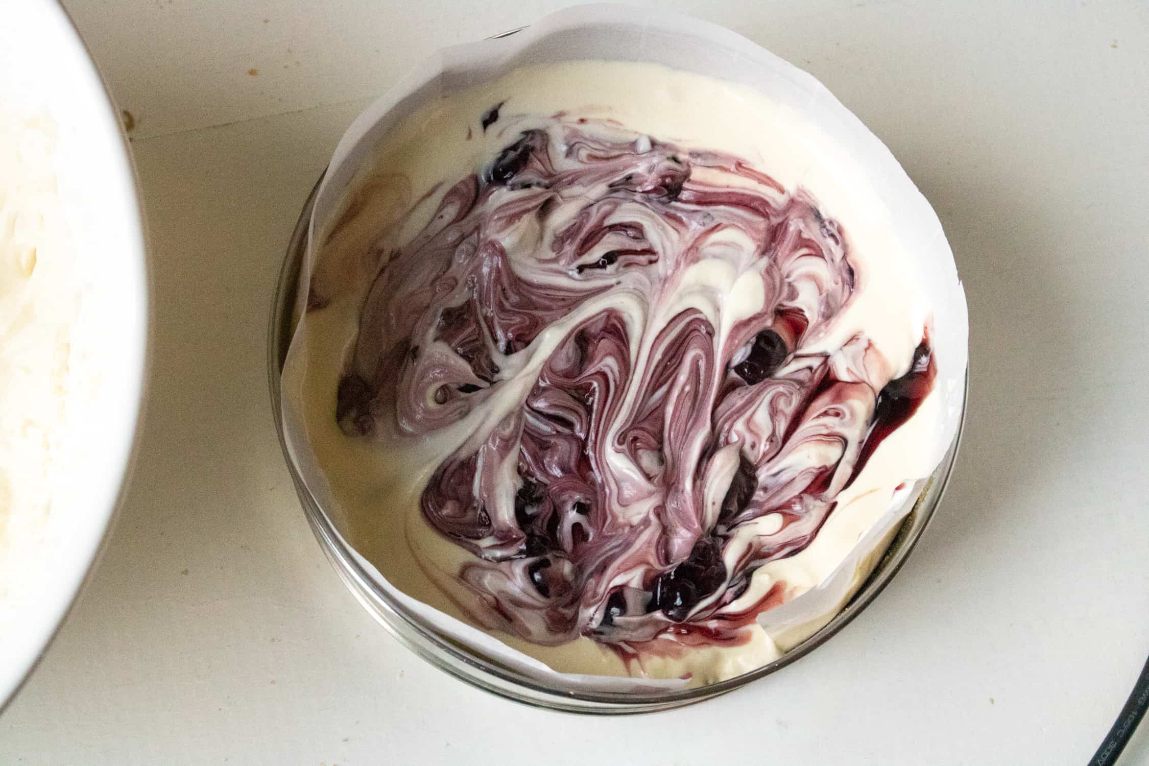 Top-down view of the unbaked Instant Pot cheesecake inside a springform pan with blackberry pie filling swirled on the top