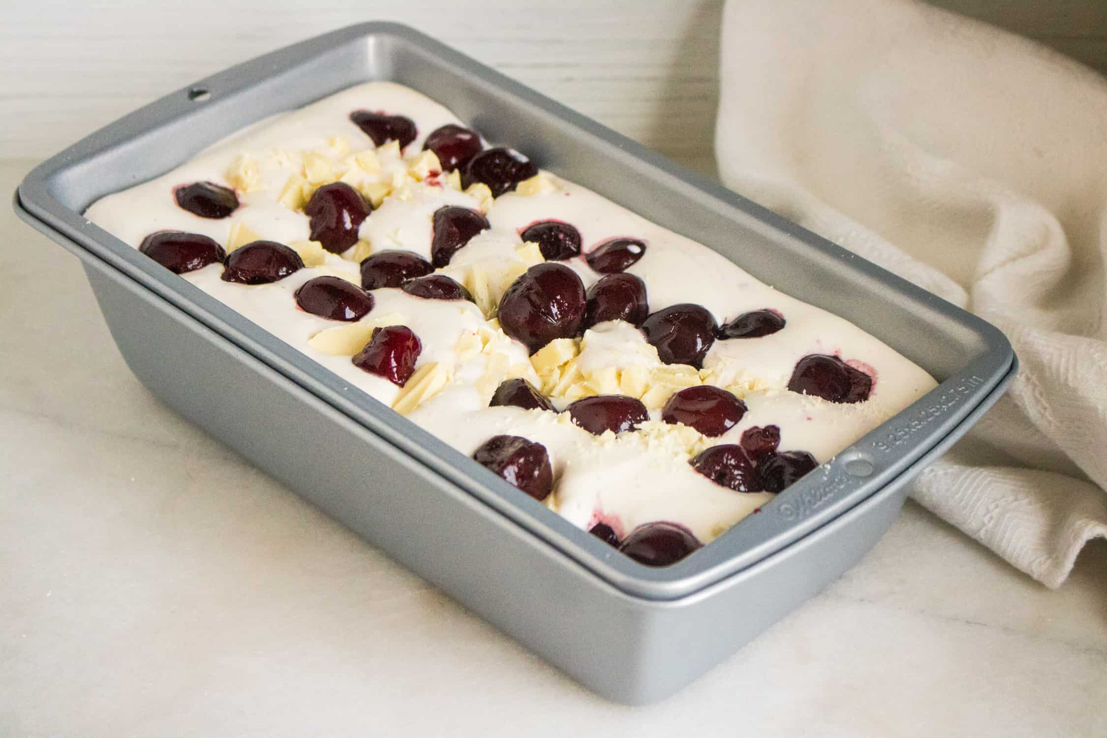 metal loaf pan filled with the no churn ice cream mixture and topped with black cherries and white chocolate chunks