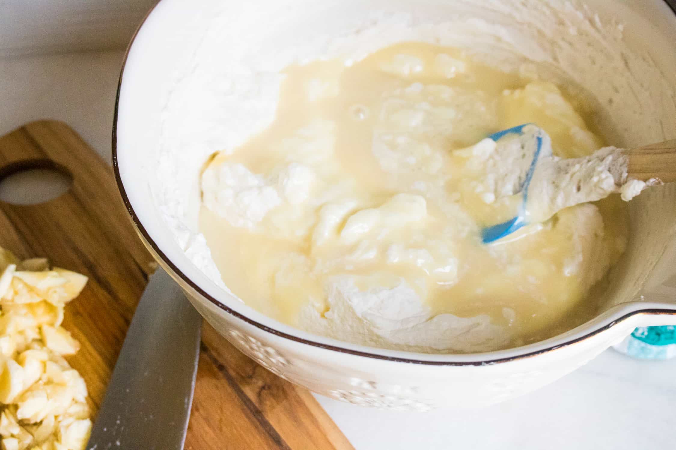 heavy whipping cream, sweetened condensed milk and vanilla being mixed together in a white bowl with a blue spatula
