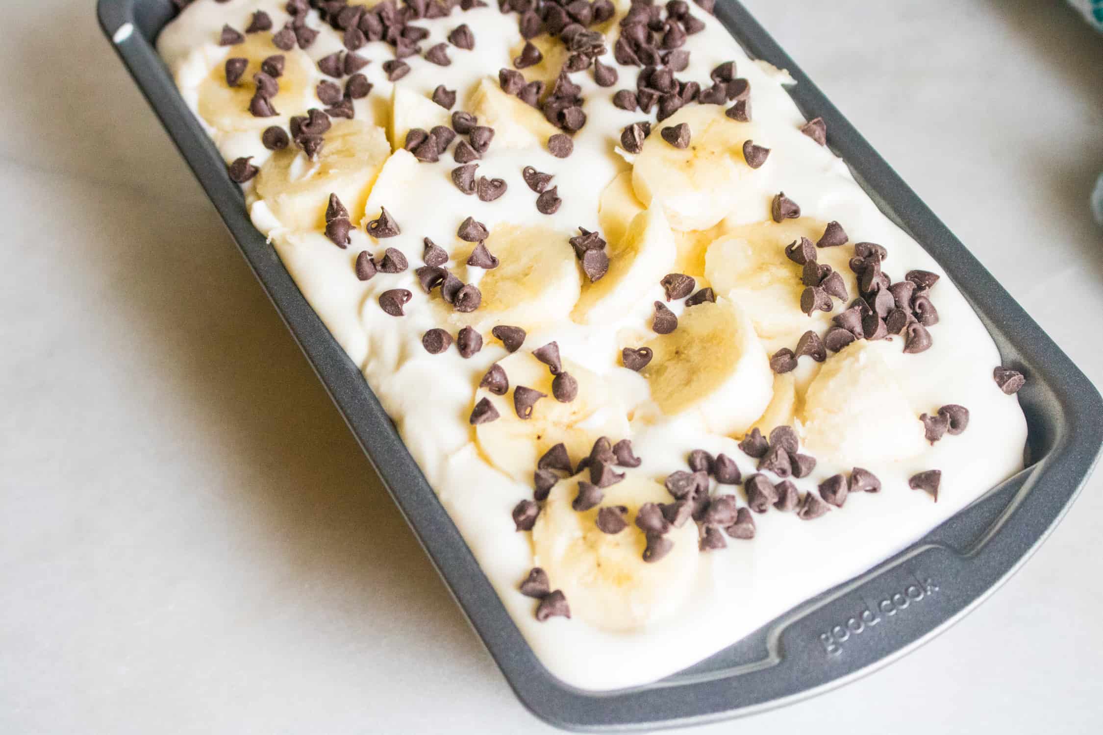 No-churn banana chocolate chip ice cream in a bread pan topped with sliced bananas and chocolate chips