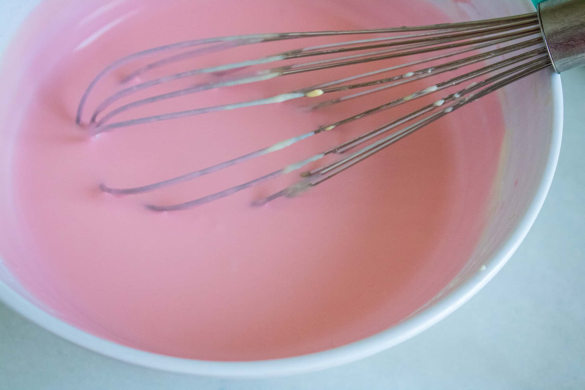 white ceramic bowl with pink mixture for bubble gum no-churn ice cream being stirred by a silver whisk