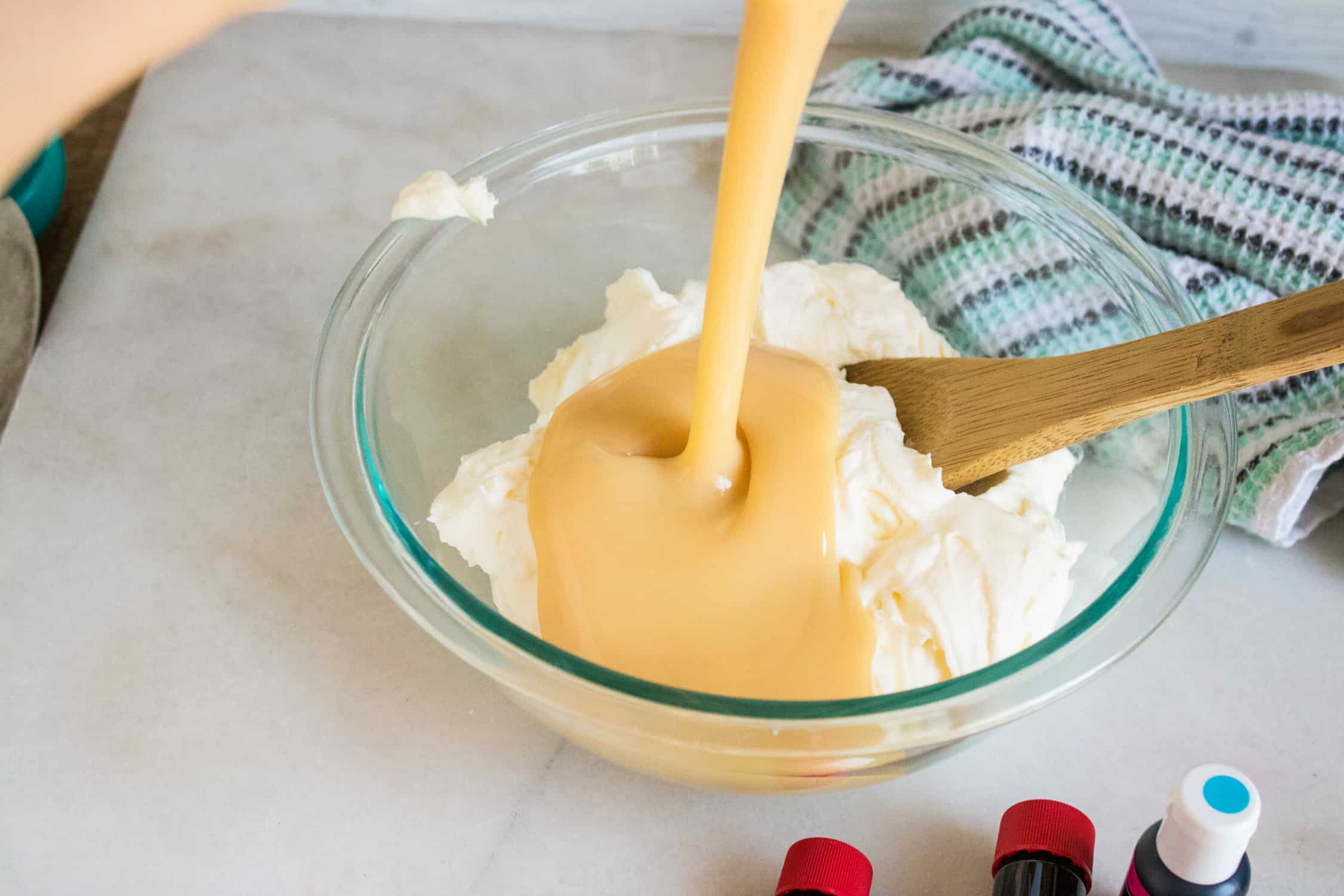 Whipped cream in bowl with sweetened condensed milk being poured on top.