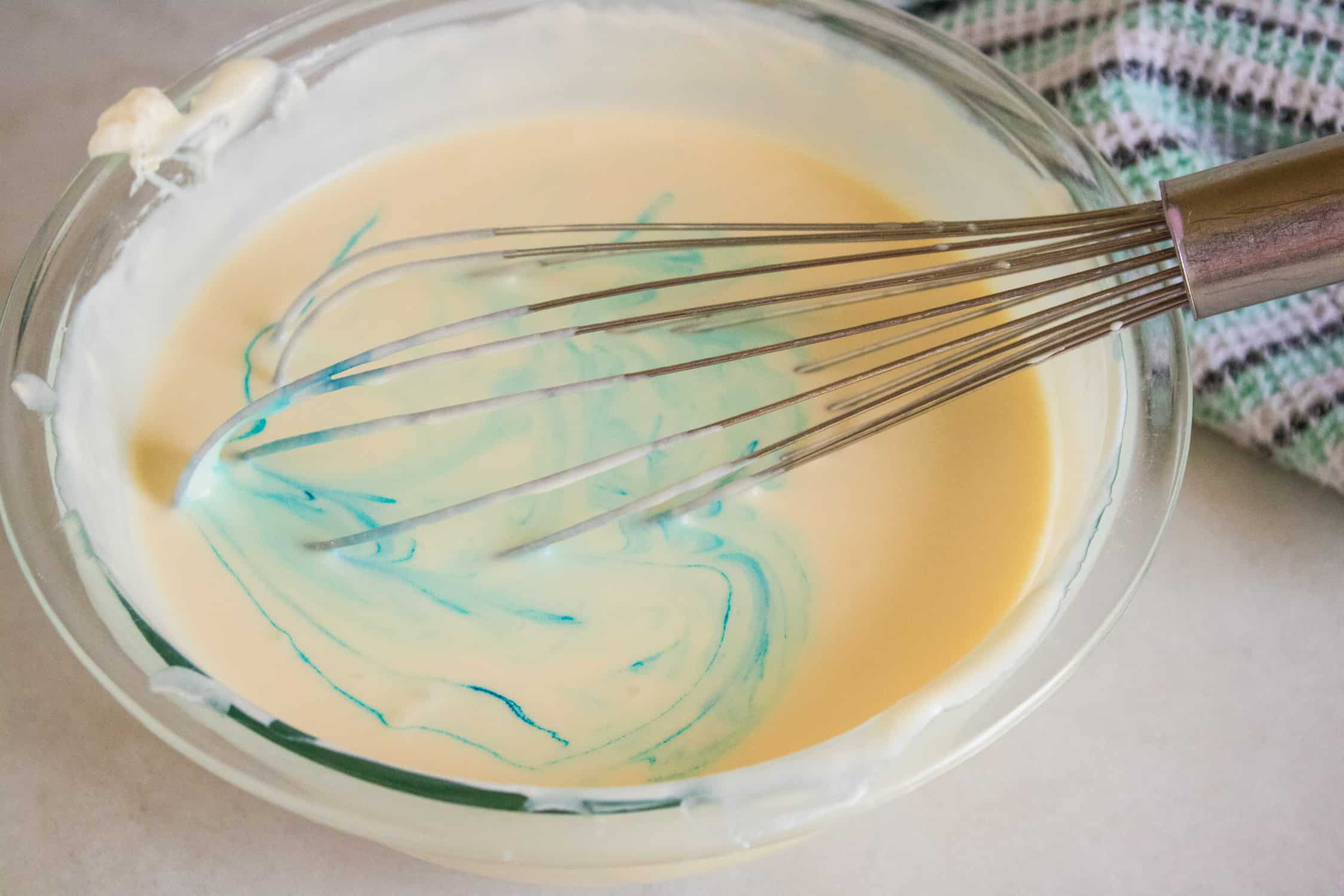 Ice cream mixture in bowl with blue food coloring being whisked in.
