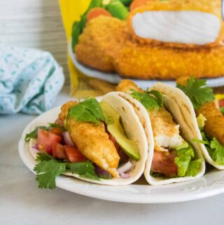 three fish tacos with pico sauce served on a white plate set in front of a bag of Gortons crunchy breaded fish fillets
