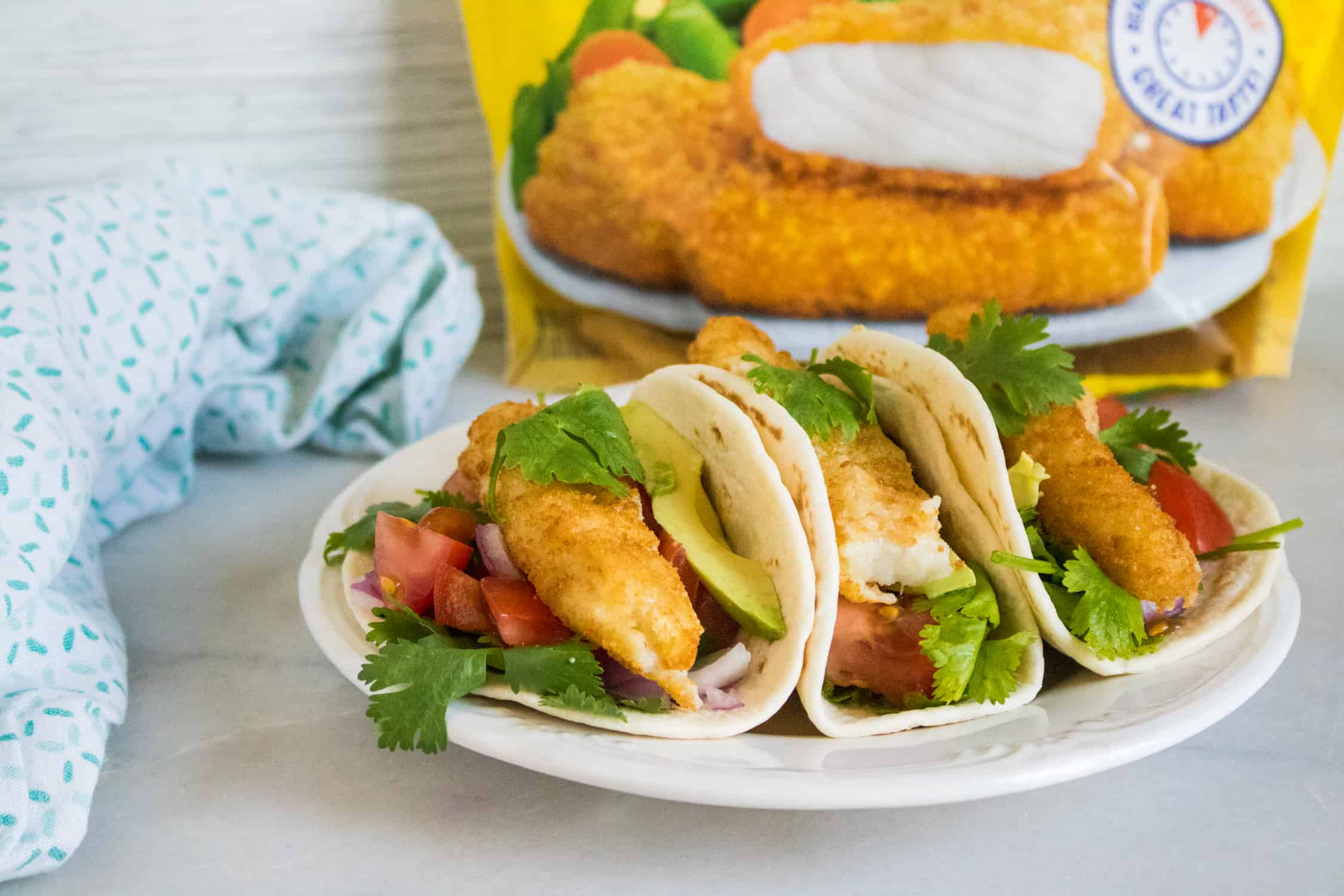 three crunchy fish tacos served on a white plate sitting in front of a bag of Gorton's Crunchy Breaded Fish Fillets
