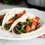 Instant Pot Refried Beans served in flour tortillas and garnished with lettuce and tomatoes