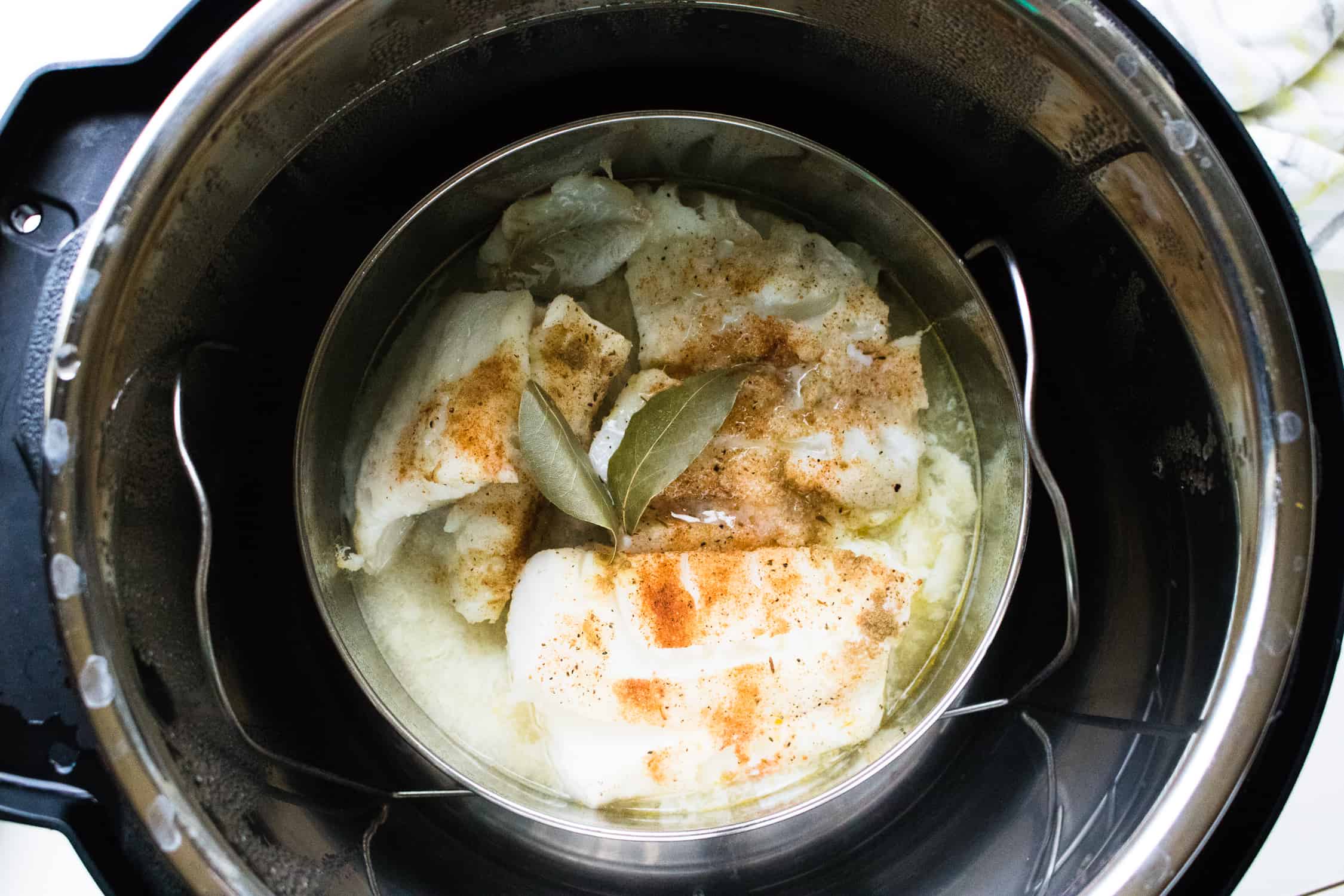 looking down into the instant pot at instant pot trivet with cod and bay leaves inside for instant pot easy fish tacos