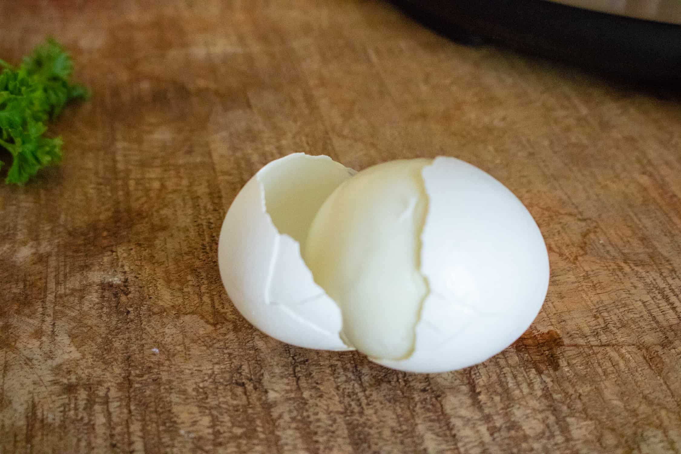 one completed Instant Pot Hard Boiled Egg with half of the shell peeled off sitting on wooden table with sprig of parsley next to it