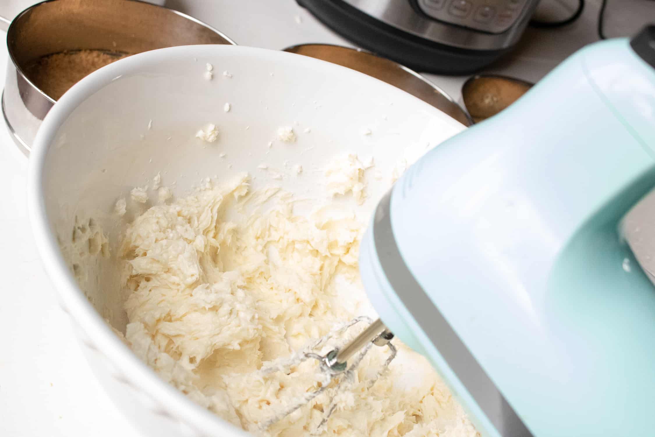 instant pot cheesecake ingredients in a large white bowl being mixed with a light blue electric hand mixer