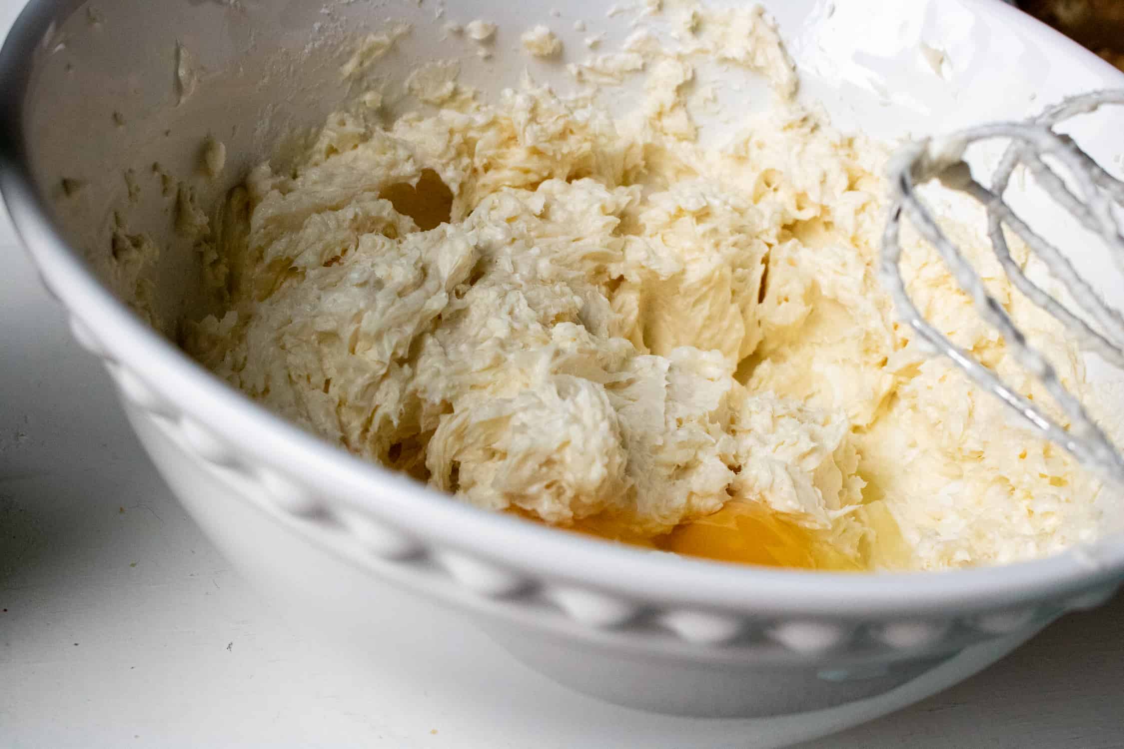 close-up view of eggs being added to the instant pot cheesecake mixture in a large white bowl