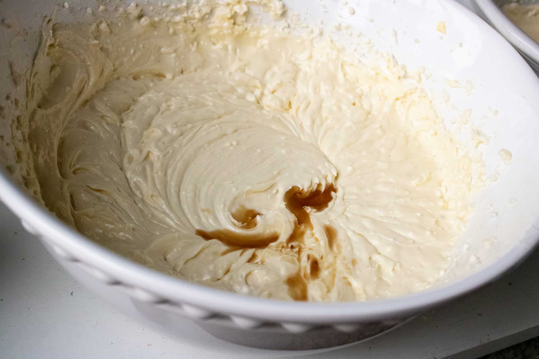vanilla extract being added to the instant pot classic cheesecake ingredients inside a white bowl
