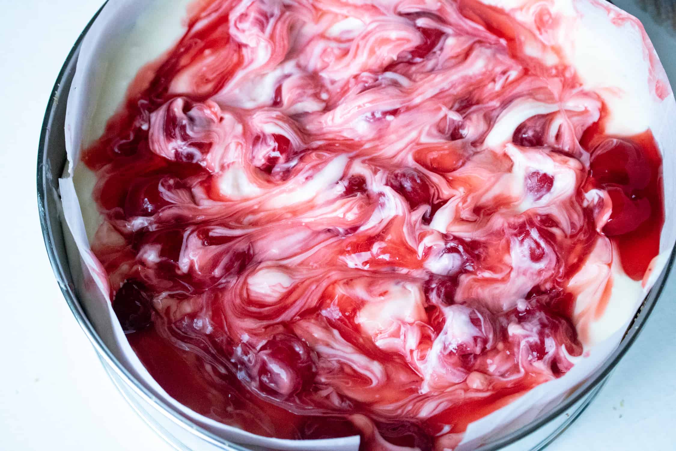 Dessert in a springform pan with cherry pie filling swirled on top