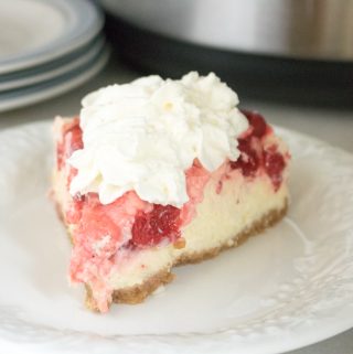 A slice of Instant Pot Cherry Swirl Cheesecake served on a white plate with the Instant Pot in the background
