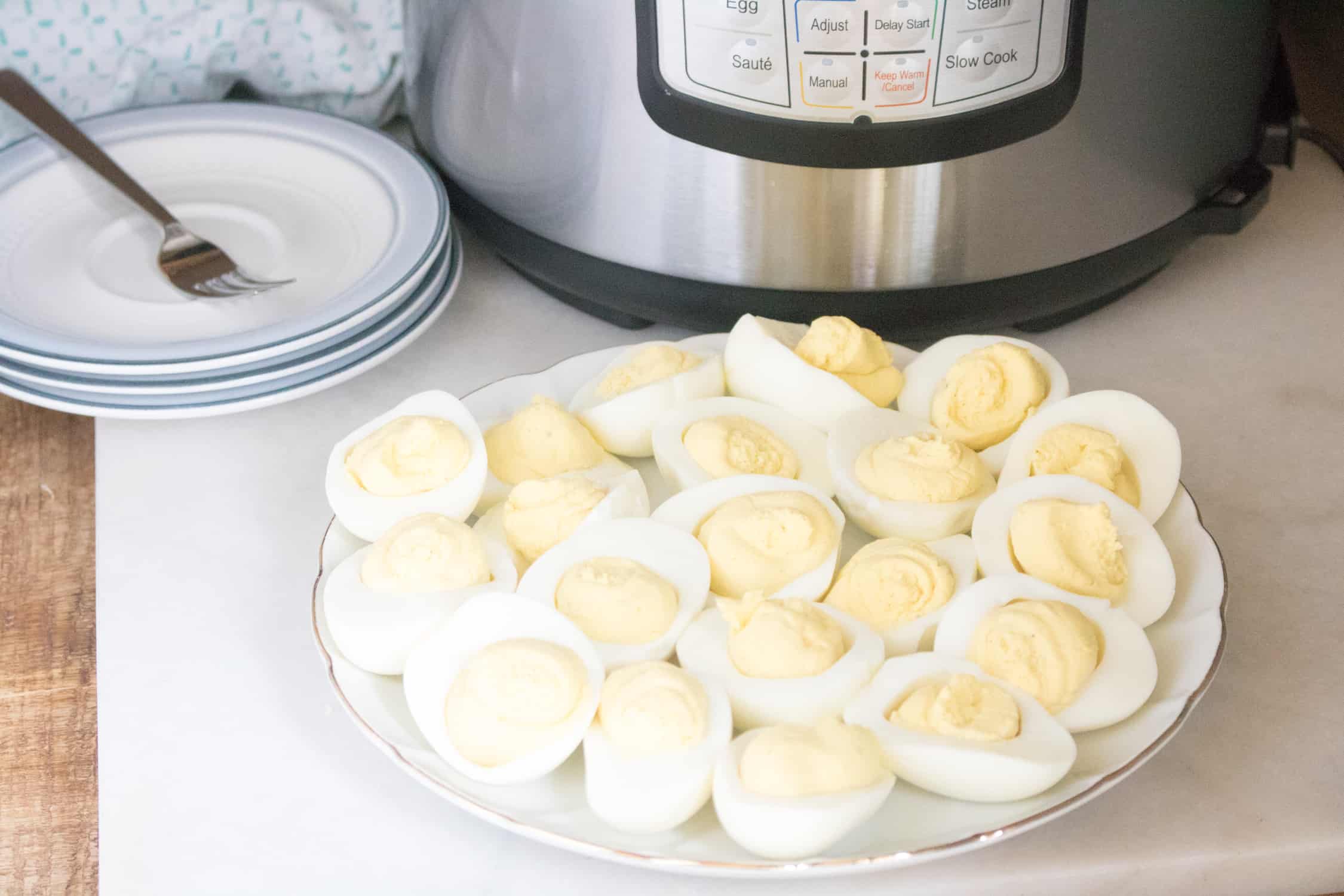 finished instant pot deviled eggs on white plate with additional white and blue plates in background next to instant pot