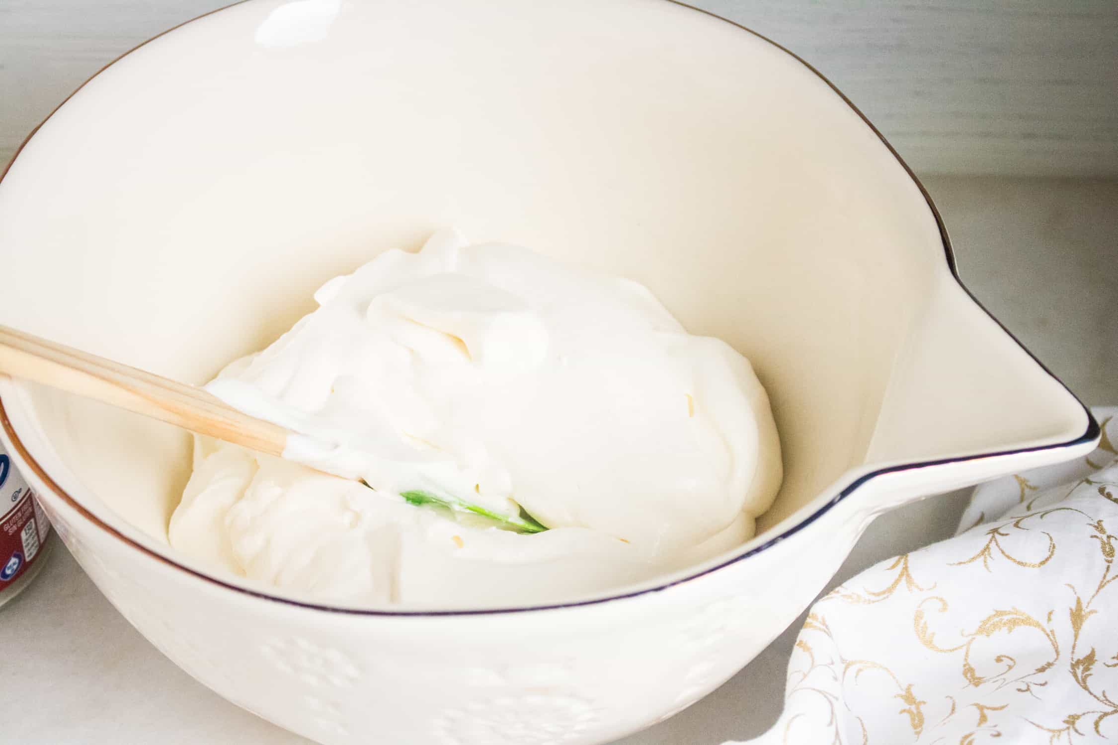 thick heavy whipping cream in a white bowl with a wooden spoon