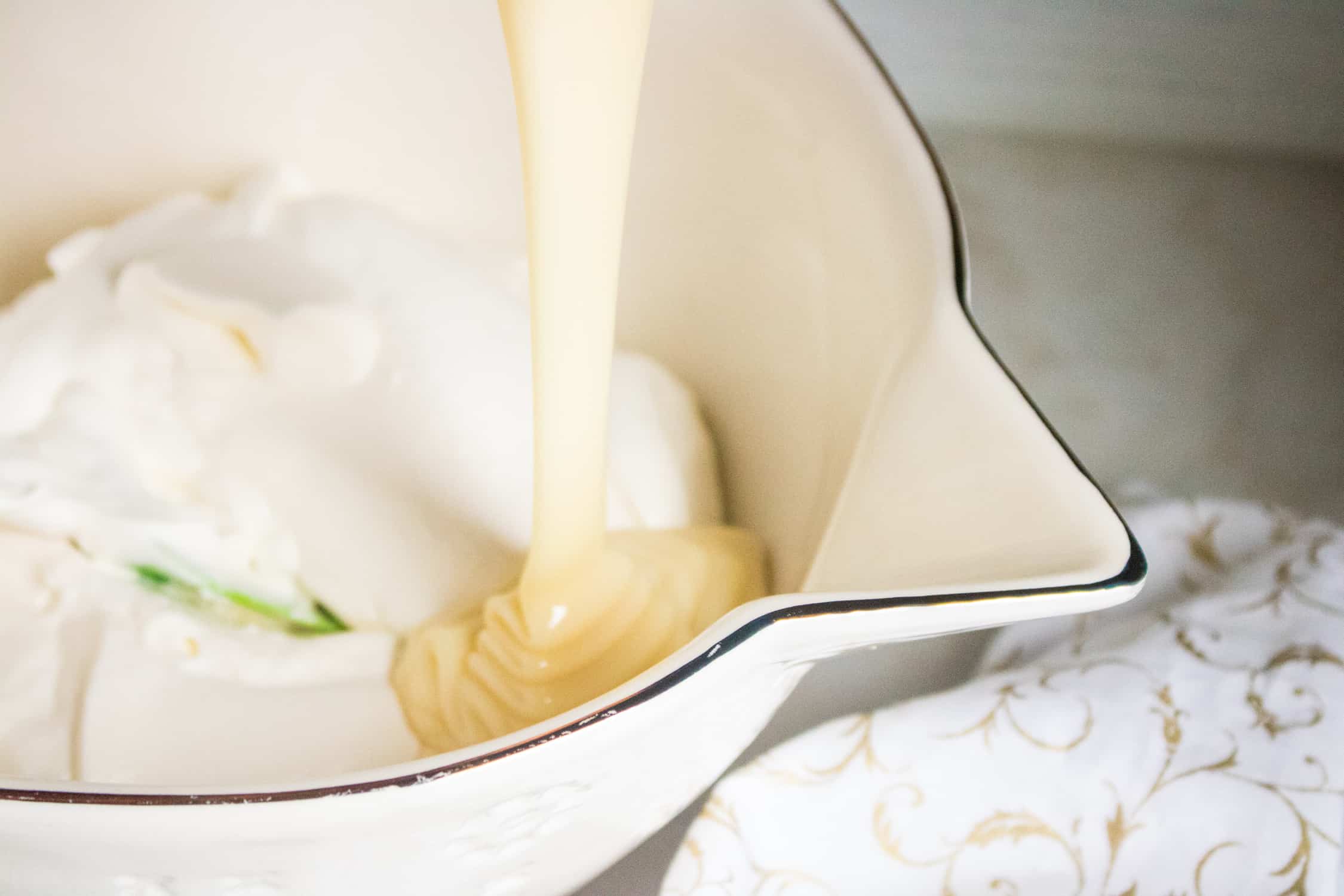 sweetened condensed milk being poured into a bowl of thick heavy whipping cream