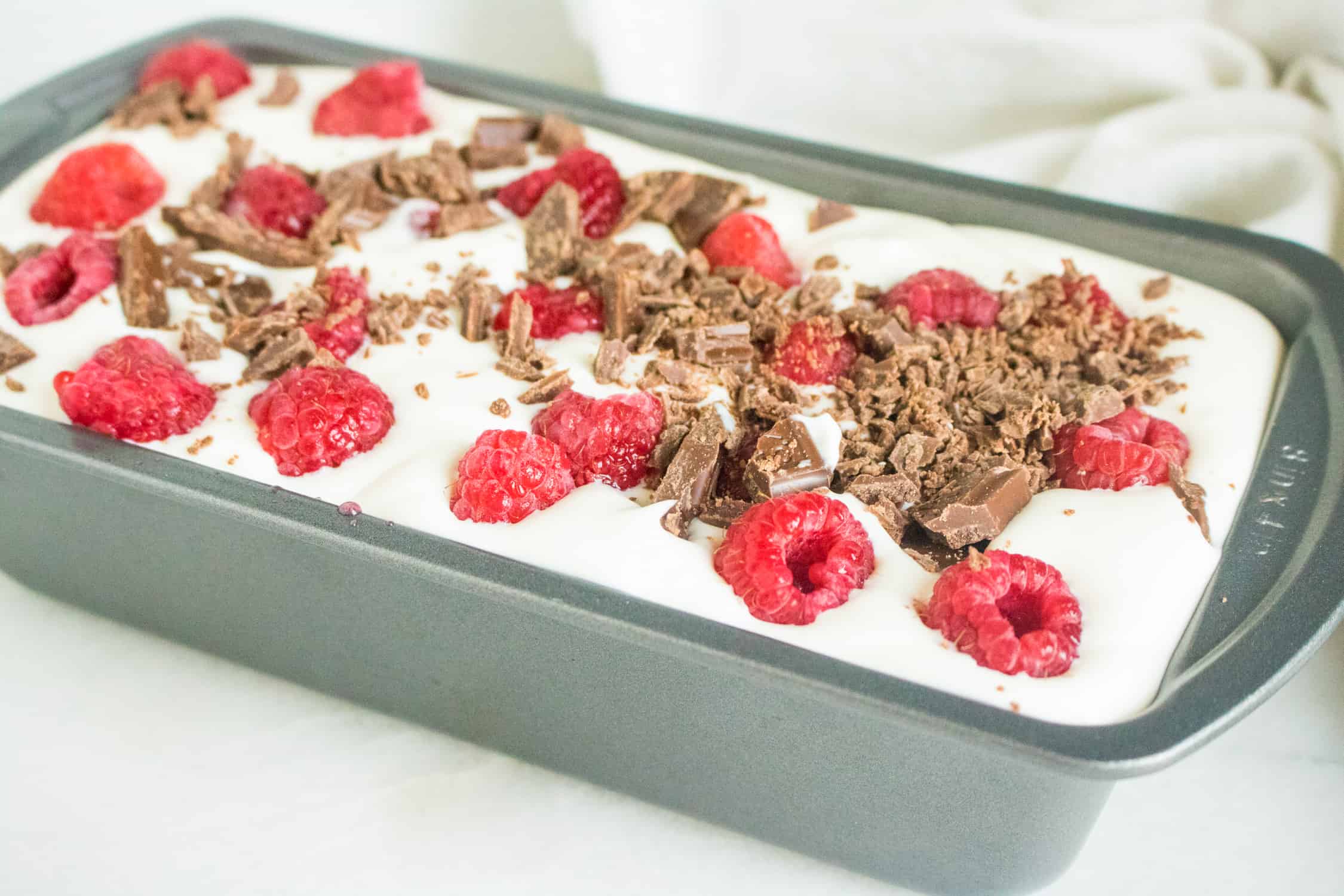 silver loaf pan filled with Raspberry Chocolate Chunk No-Churn Ice Cream base with fresh raspberries and chocolate chunks on top