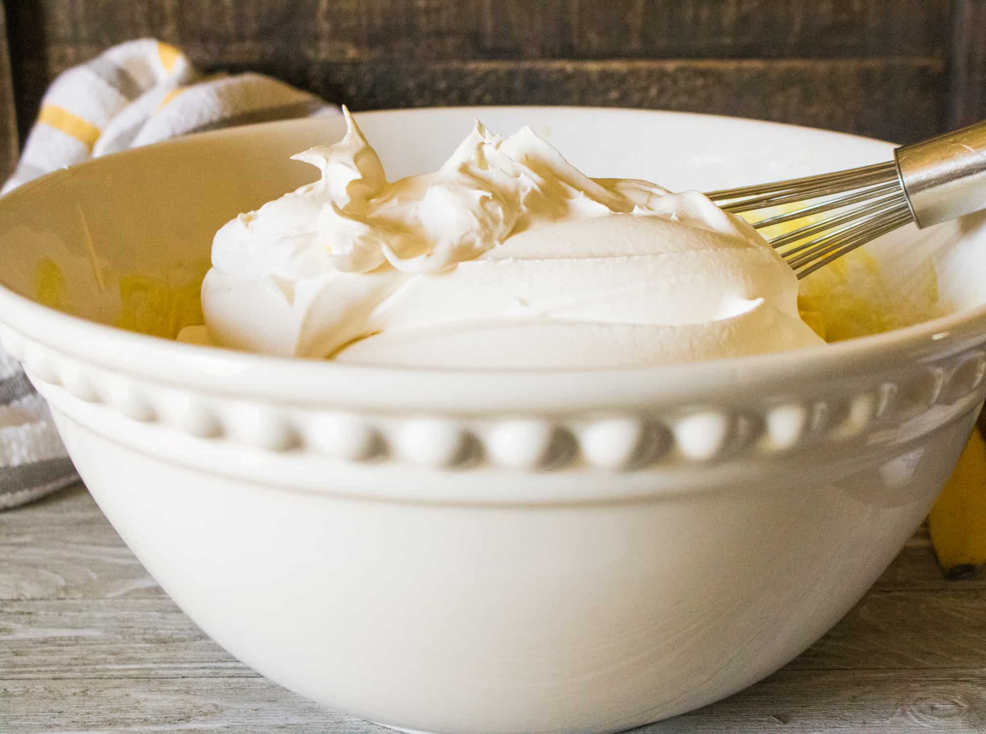 white ceramic bowl with whipped heavy cream for no-churn peanut butter ice cream in it with silver whisk