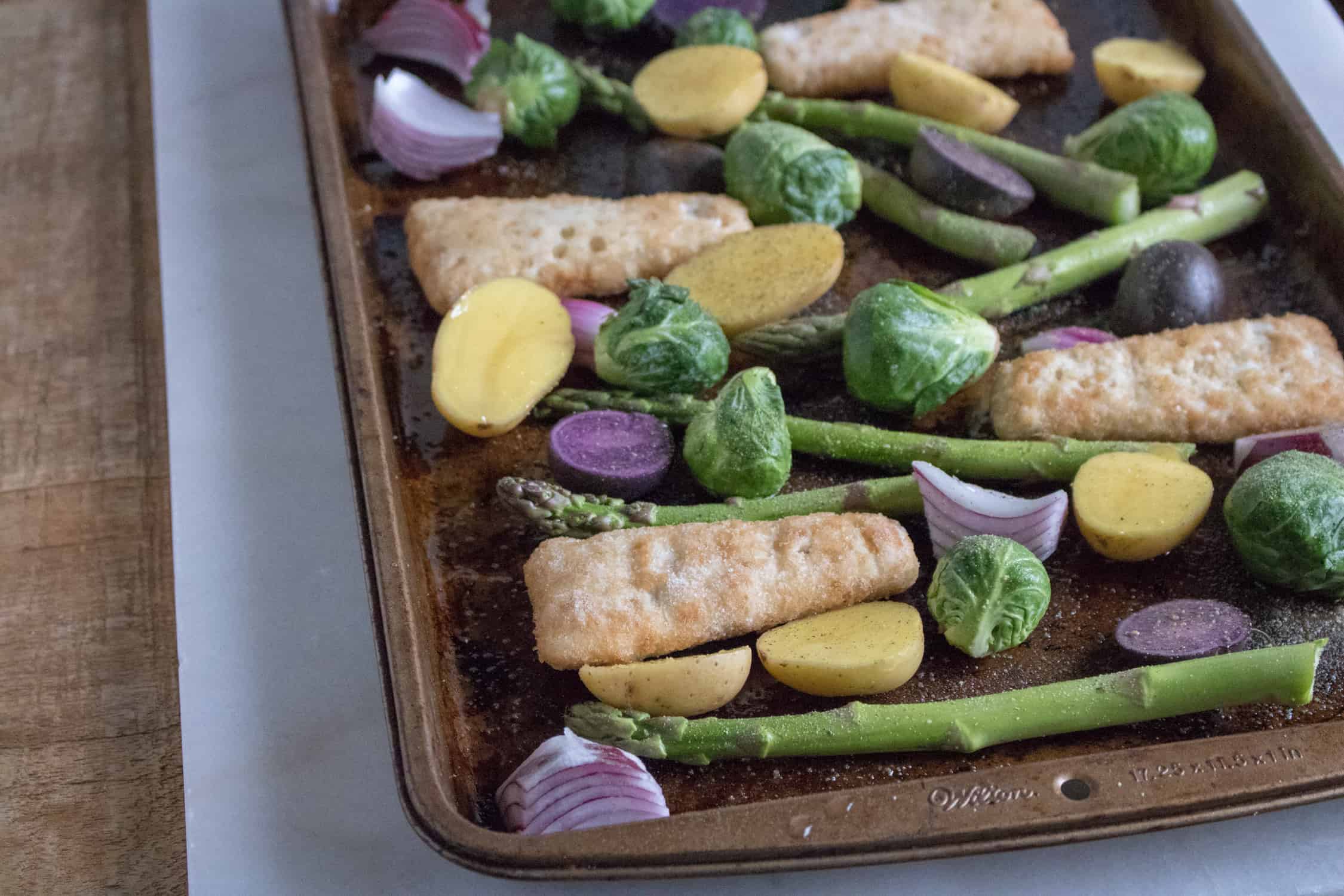 sheet pan veggies with fish fillets on a baking sheet