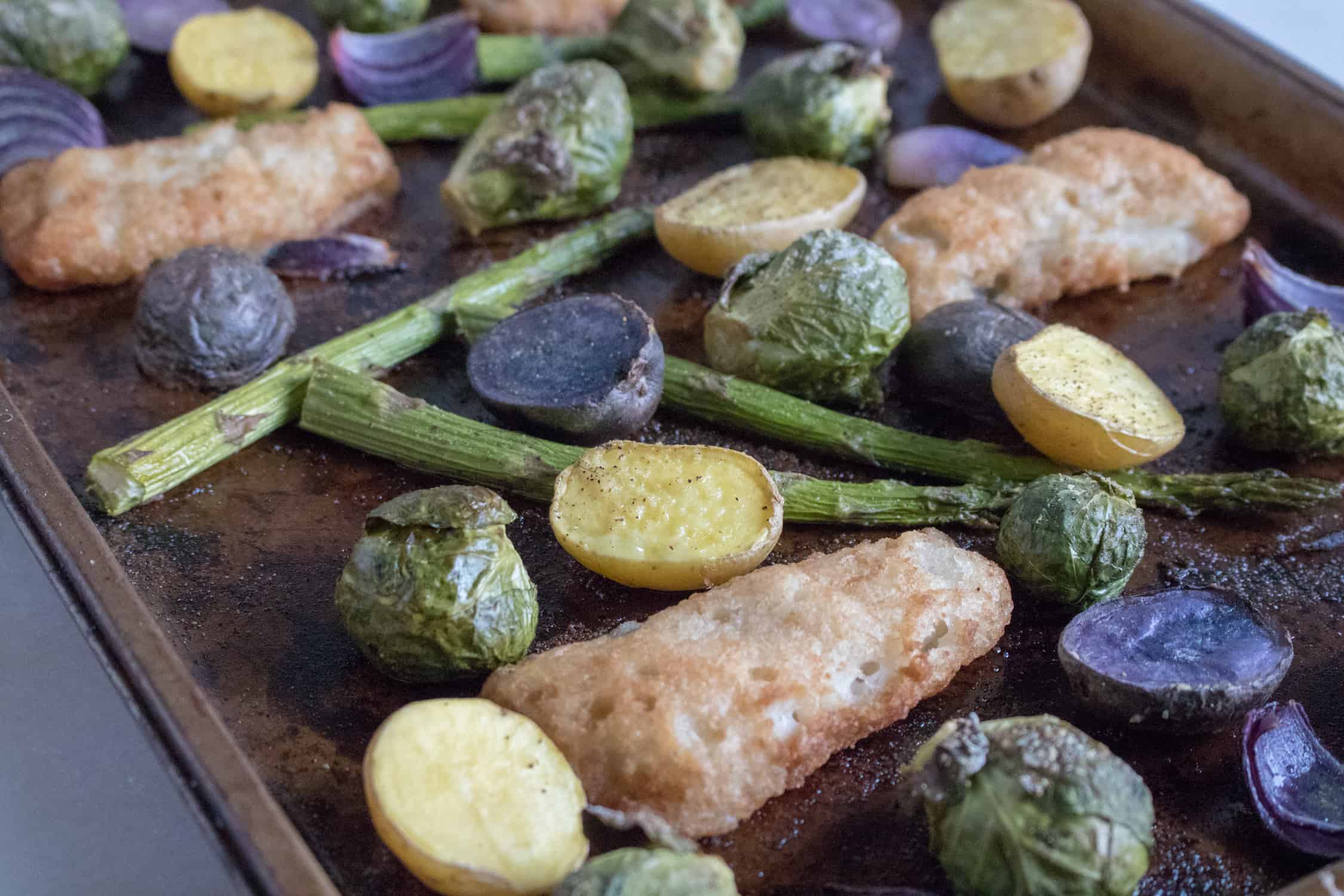 close up of the sheet pan veggies with fish fillets on a baking sheet