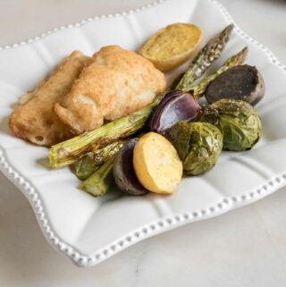 One serving of sheet pan veggies with fish fillets one-pan meal on a white dinner plate