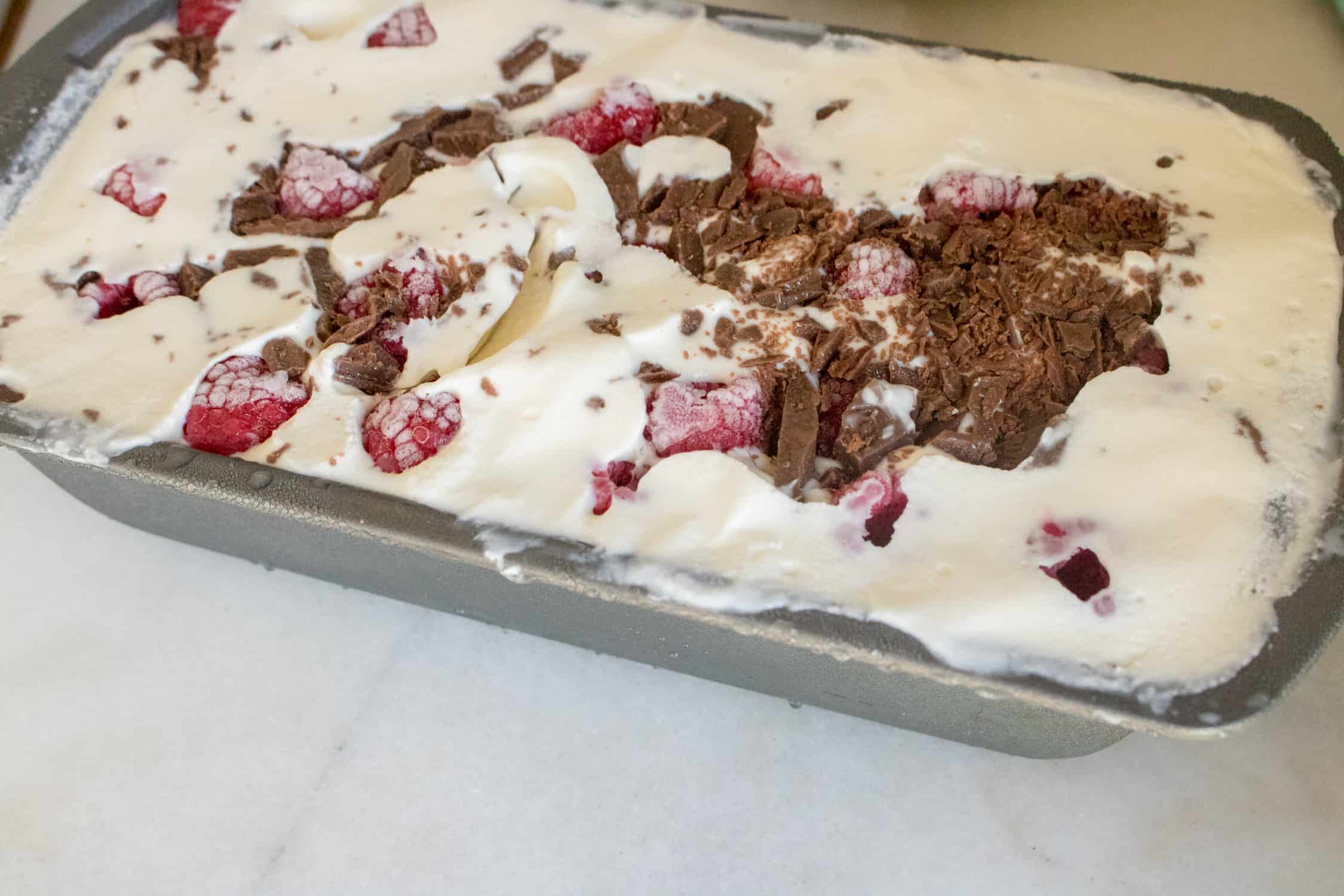 silver loaf pan filled with all ingredients for Raspberry Chocolate Chunk No-Churn Ice Cream 