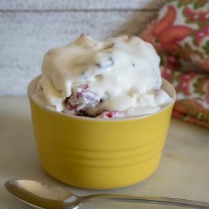 one scoop of Raspberry Chocolate Chunk No-Churn Ice Cream served in a yellow bowl with a silver spoon and a red print cloth napkin