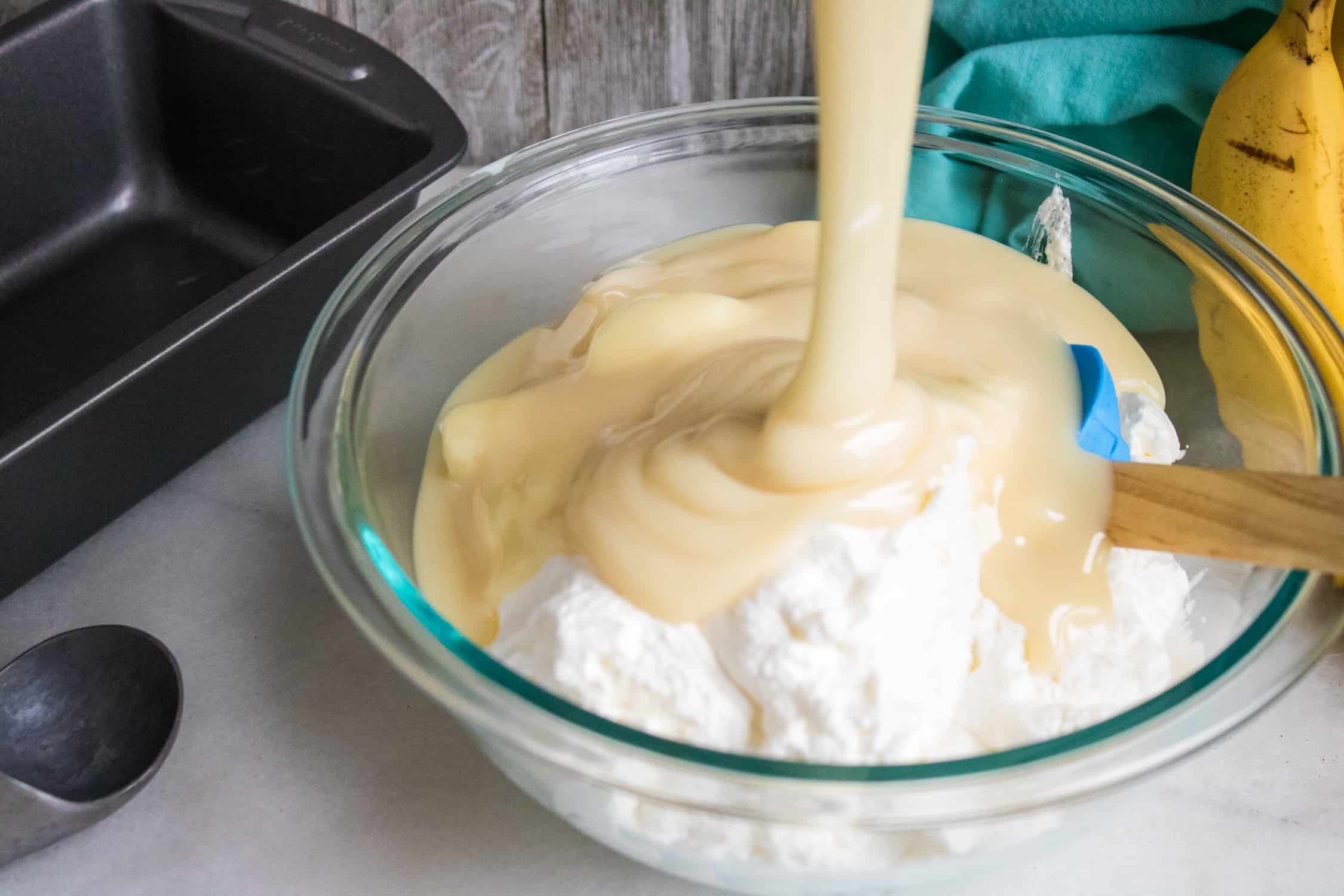 sweetened condensed milk being poured over thick heavy whipping cream in a glass bowl during the making of this easy ice cream recipe