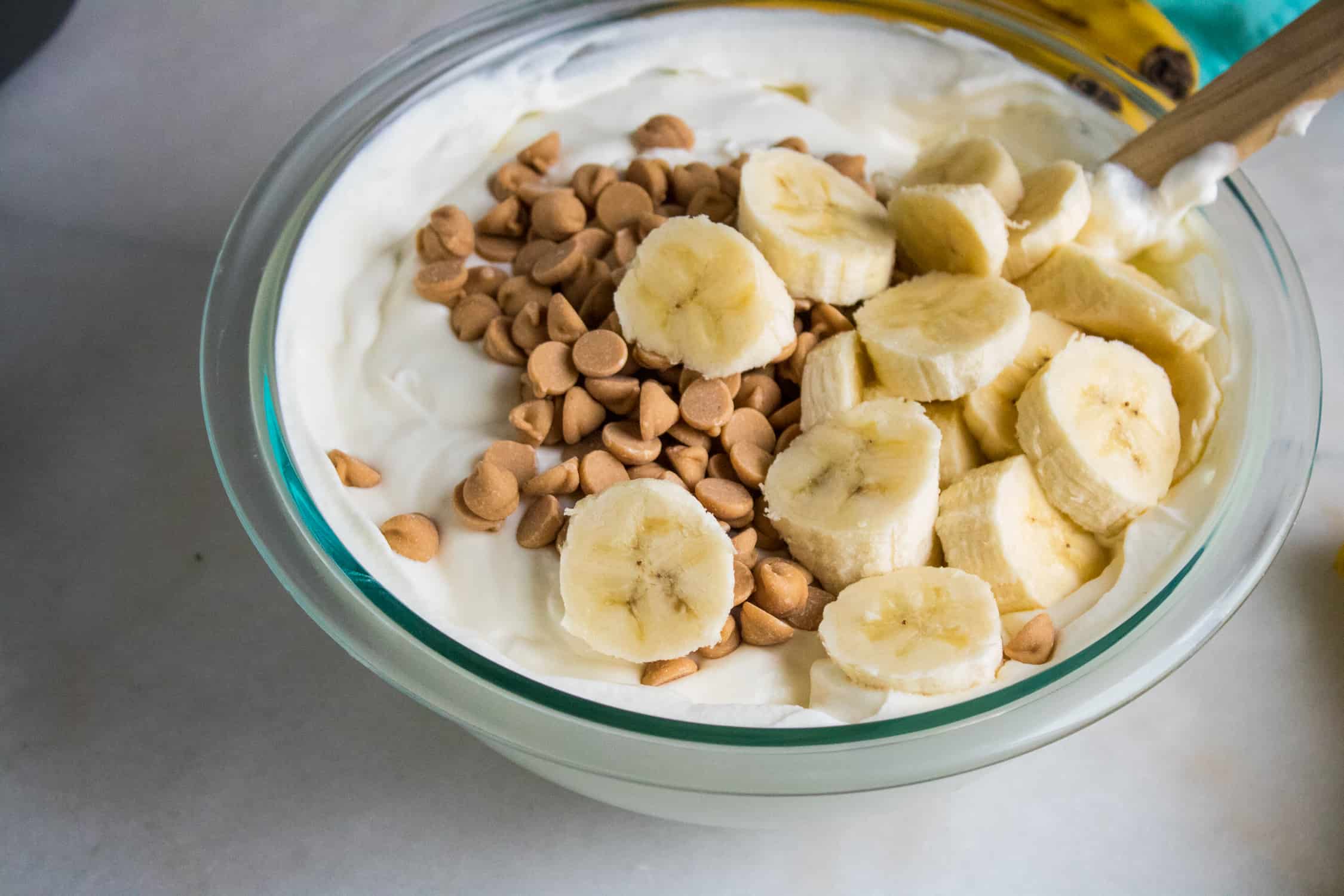 Reese's peanut butter chips and sliced bananas being mixed into a bowl of the ingredients for this no churn easy ice cream recipe