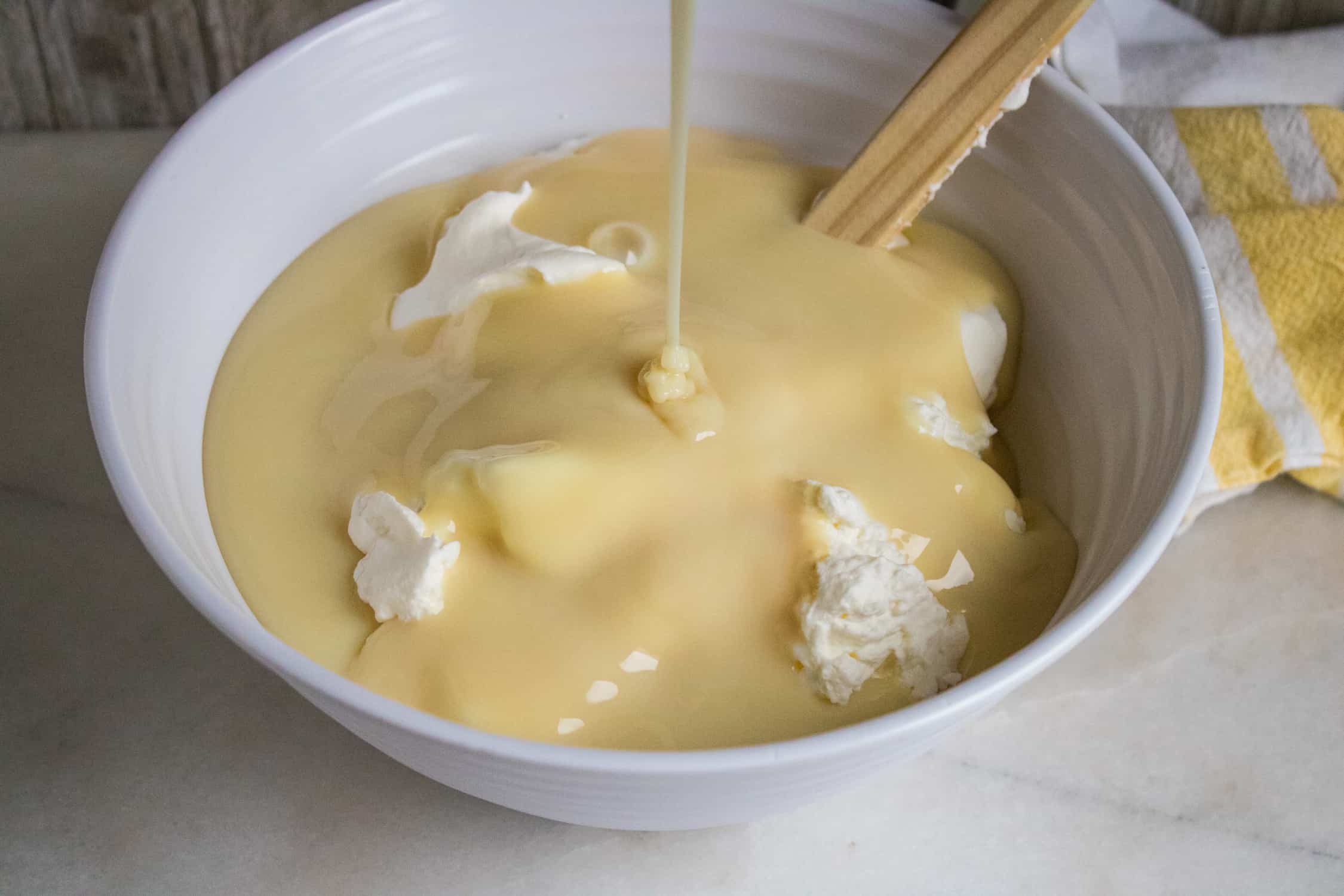 sweetened condensed milk being poured into a bowl of thick, heavy whipping cream