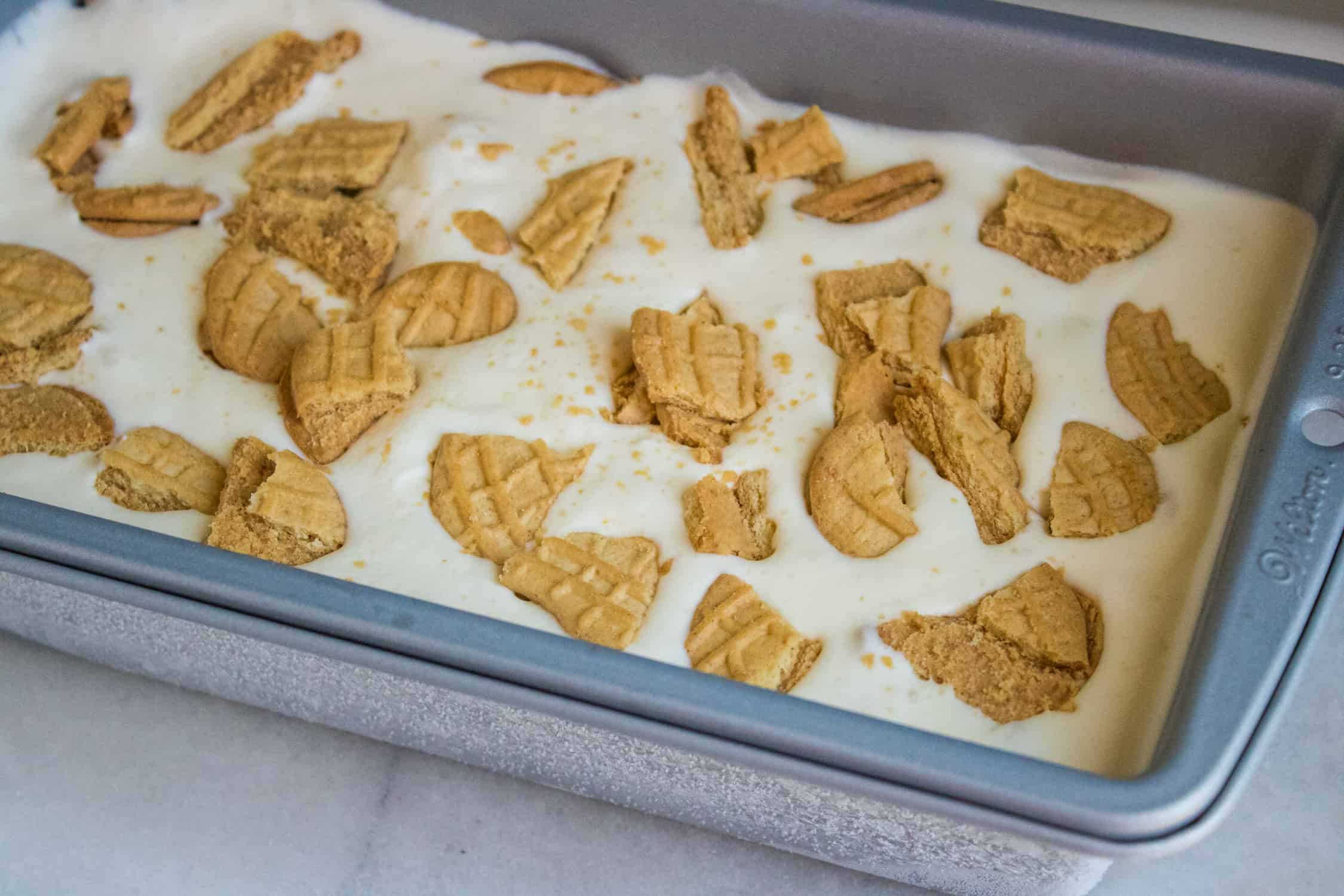 Nutter butter no churn ice cream in loaf pan with pieces of cookie on top before freezing