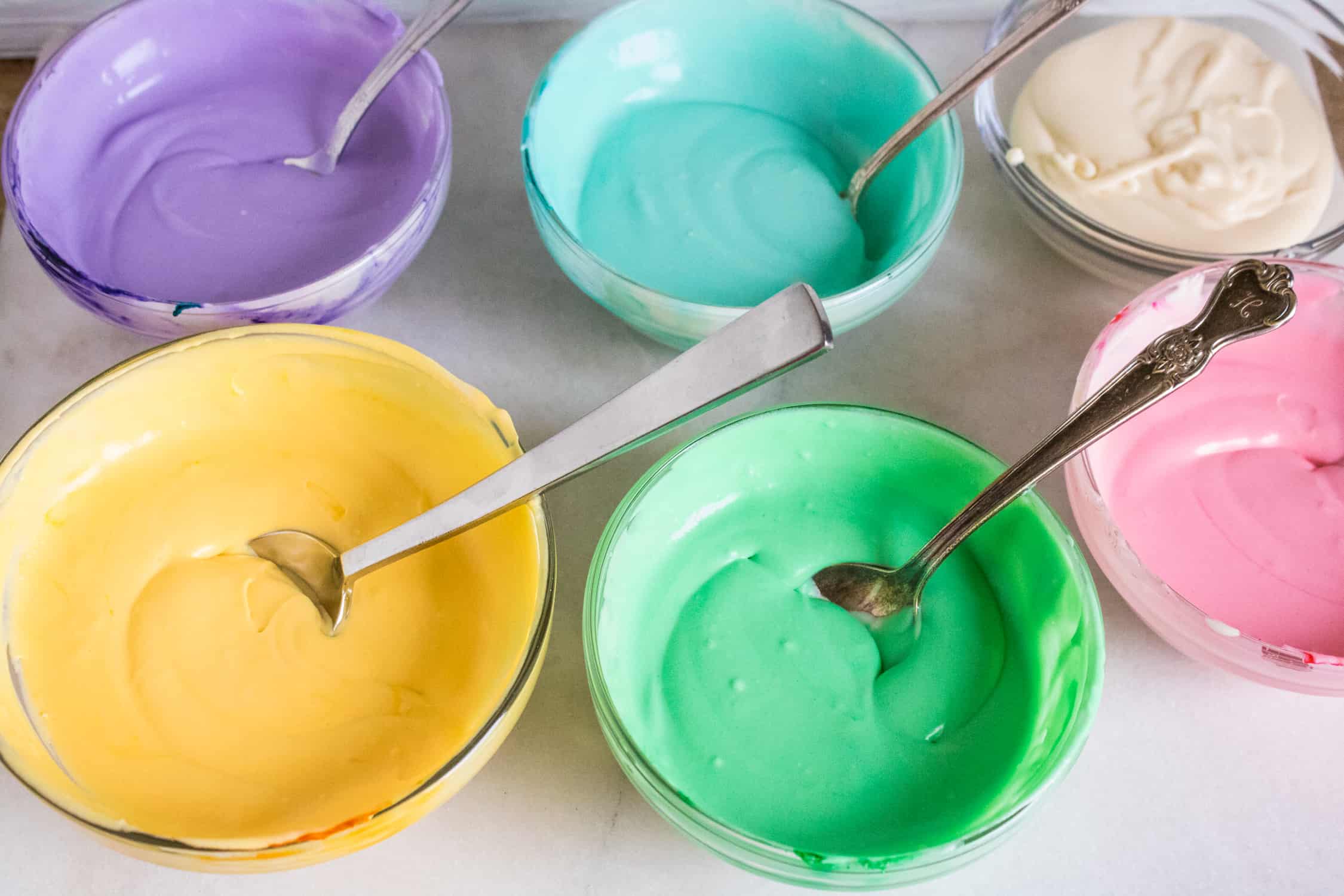 Birthday cake ice cream mix divided into 5 small mixing bowls and colored with purple, yellow, blue, green and pink food coloring