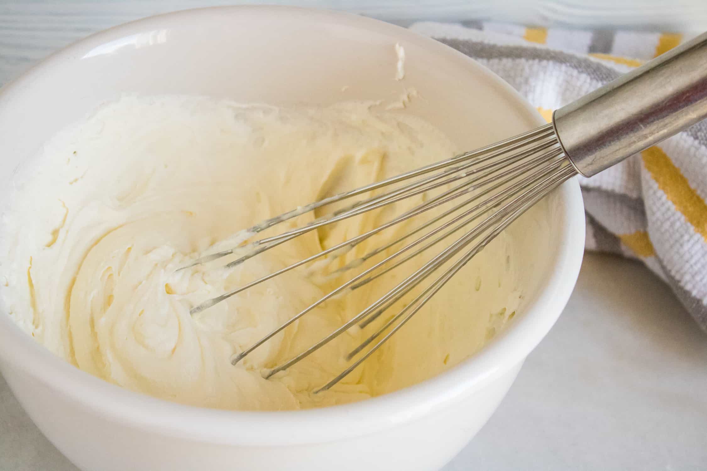 ingredients for Orange Creamsicle No-Churn Ice Cream being folded together with a whisk inside a white mixing bowl