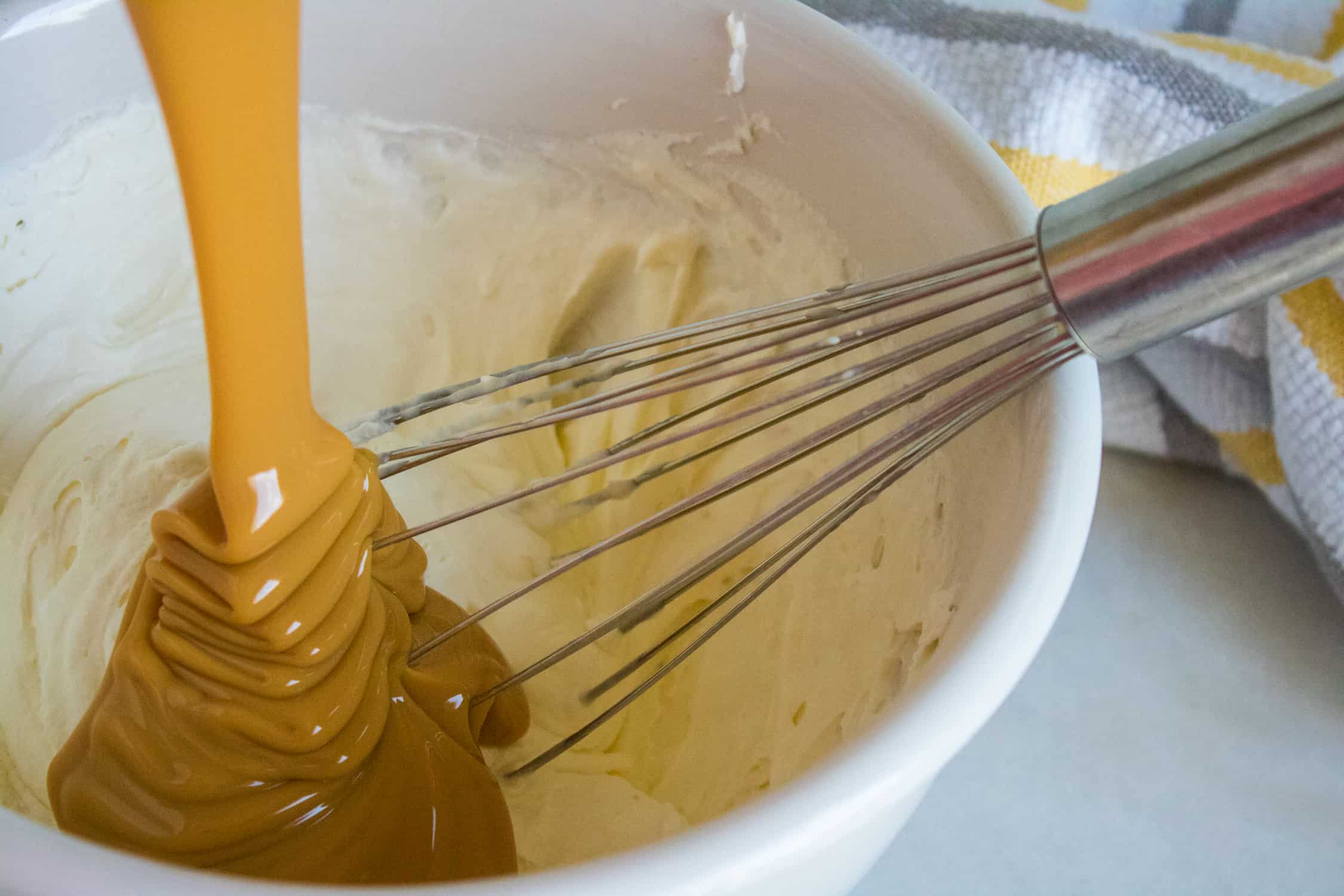 condensed milk being poured on top of whipped cream inside a white mixing bowl