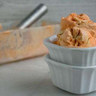 Glass container of Orange Creamsicle No-Churn Ice Cream in front of a white square ceramic ramekin filled with two scoops of the ice cream