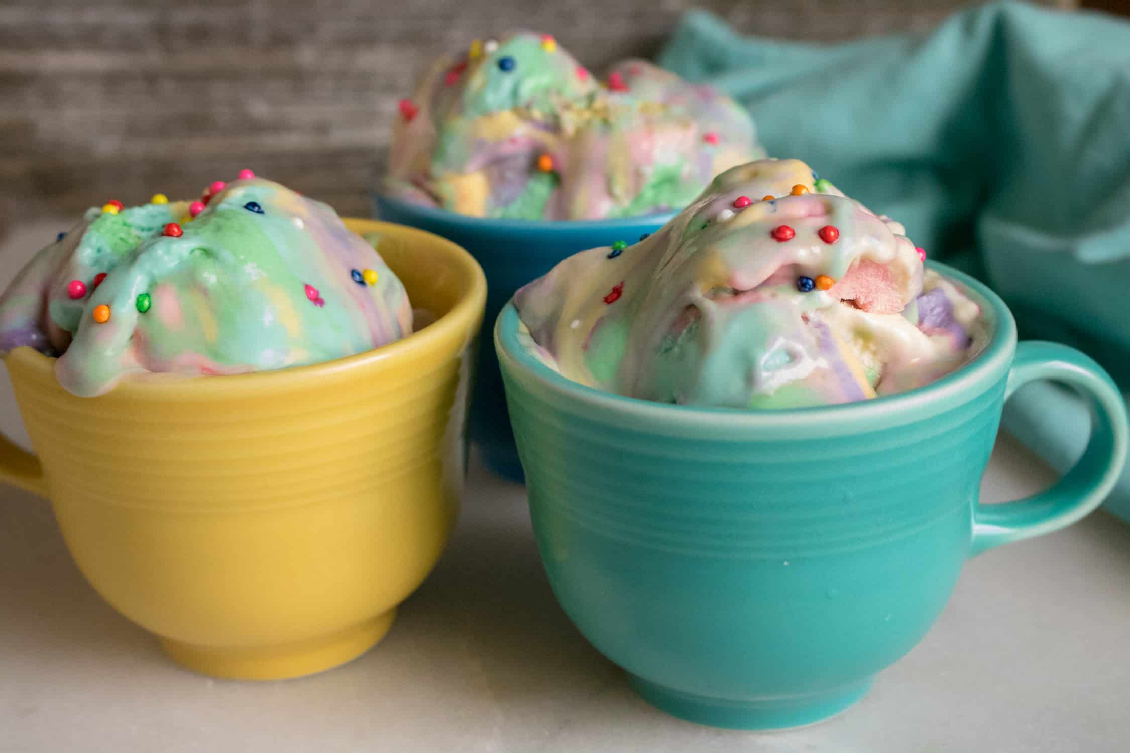 Birthday Cake No-Churn ice cream served in three different colored mugs and topped with rainbow sprinkles