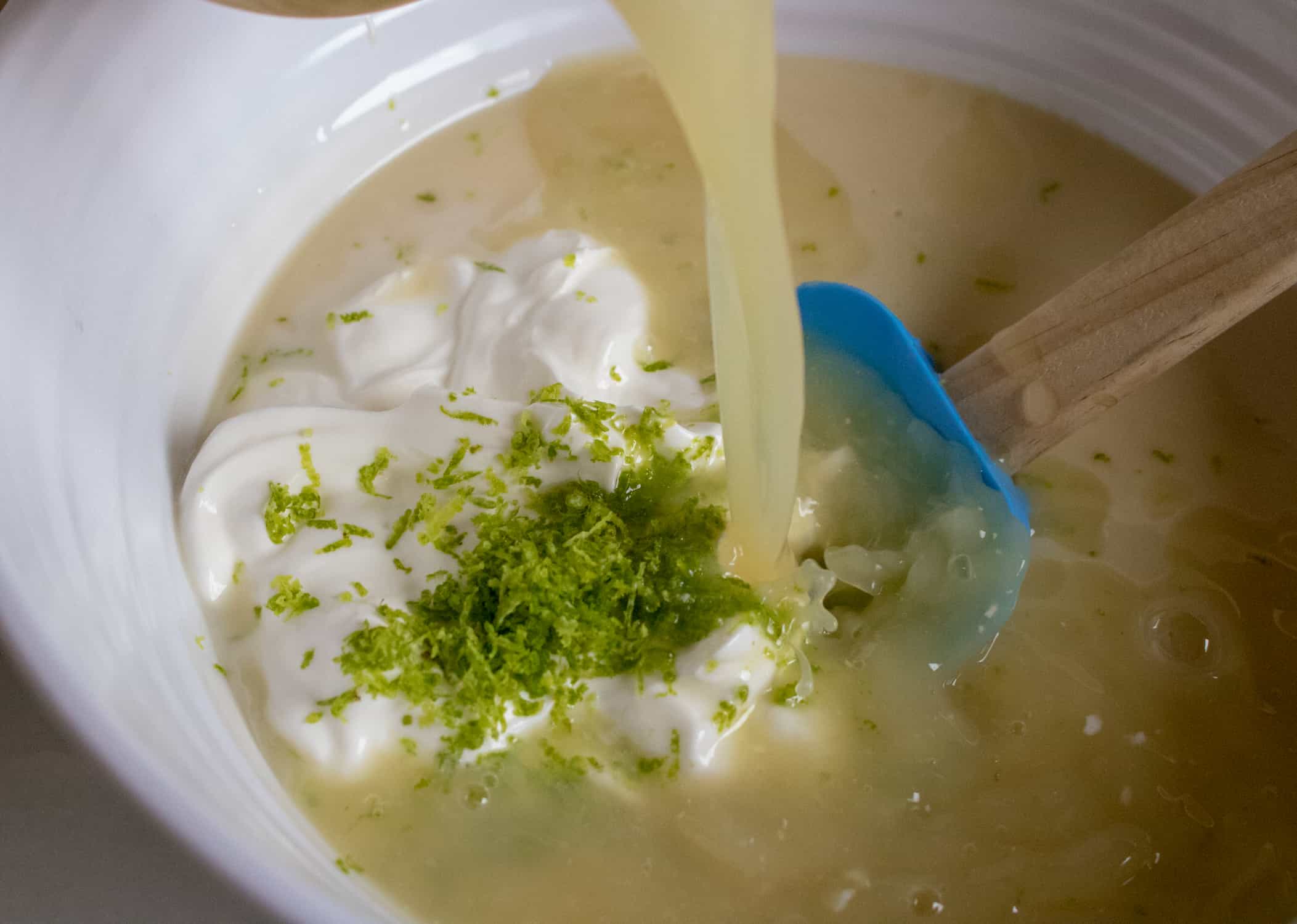 Lime zest and juice being poured into a white bowl with sweetened condensed milk and sour cream