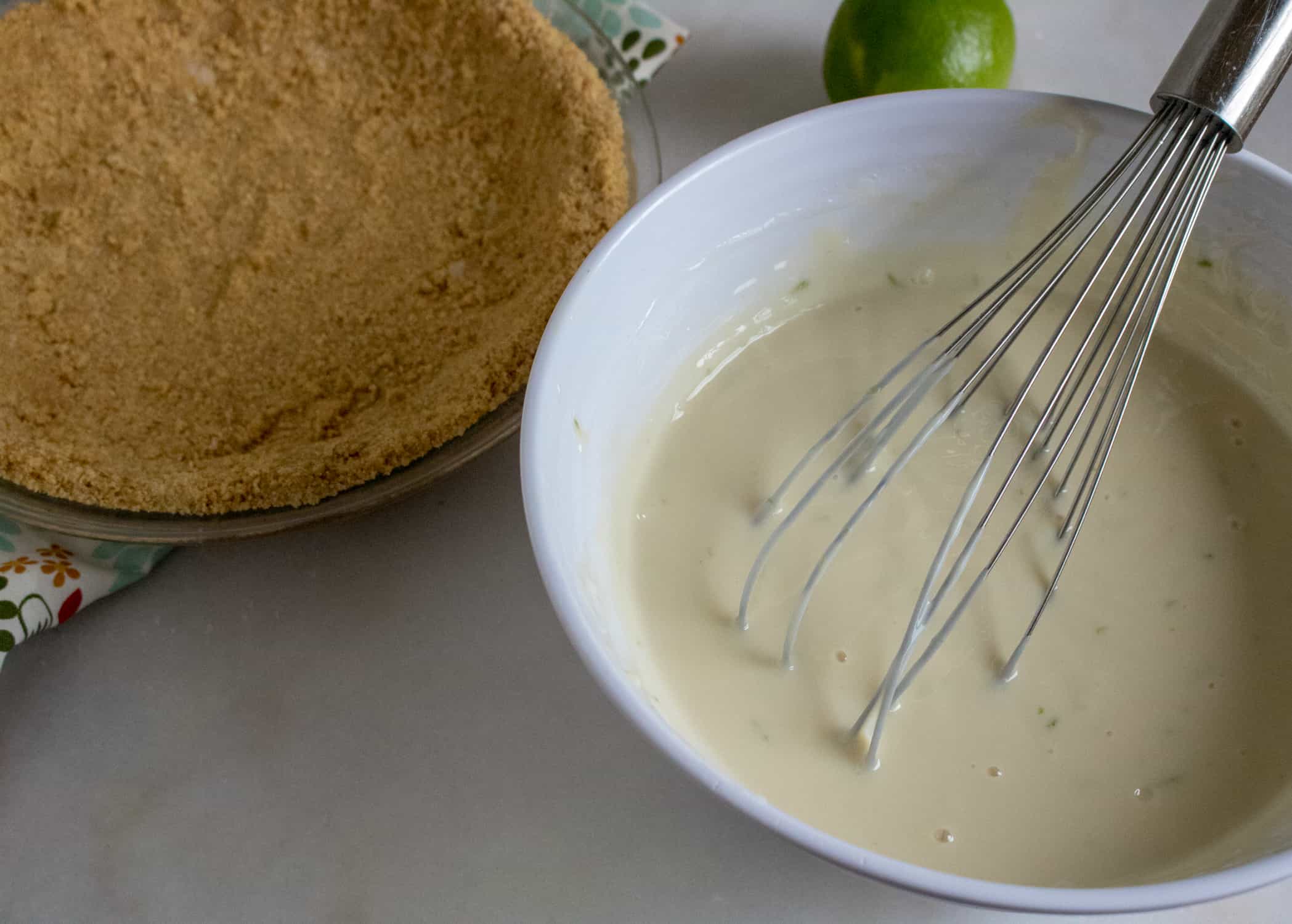 Graham cracker crust and filling mixture in a bowl with a whisk used to mix ingredients.