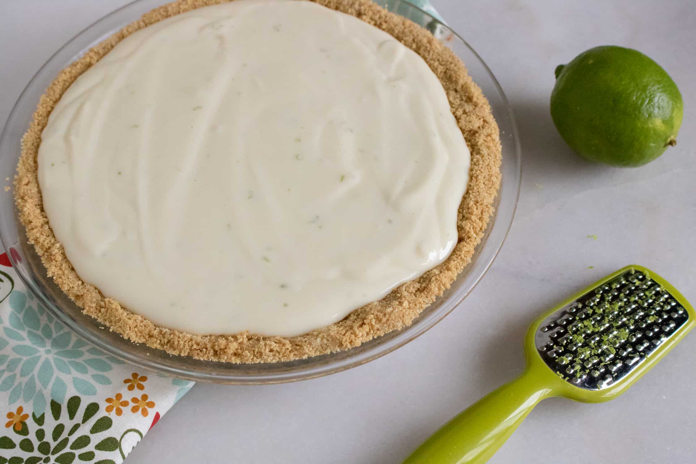 Graham cracker crust with pie filling added. Lime, zest grater and kitchen towel beside.