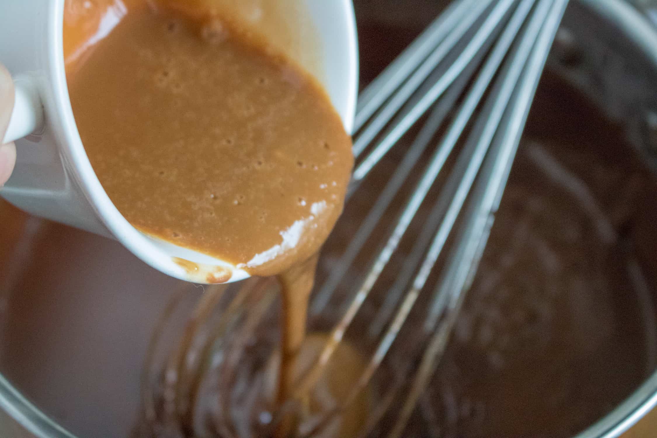 A small portion of chocolate mixture mixed in with the egg yolks being poured into the sauce pan with the chocolate cream pie filling