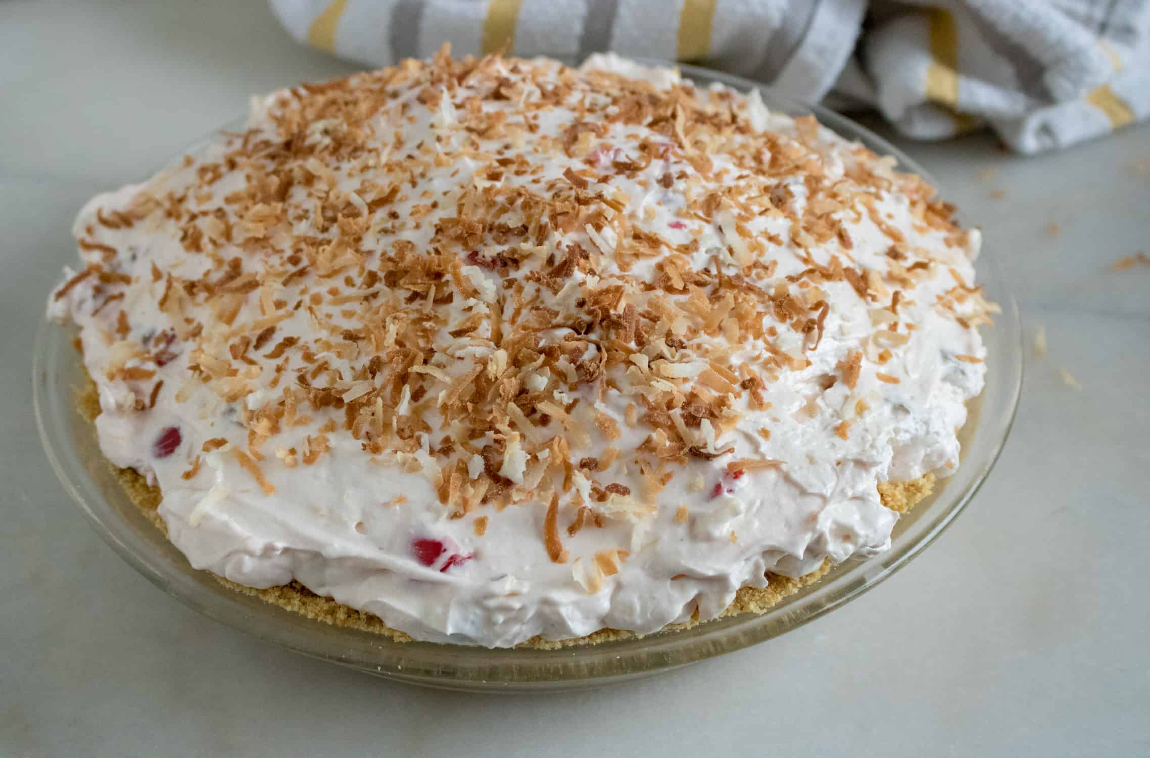 Assembled pie in a pie plate. Graham cracker crust, cream cheese mixture and whipped topping with toasted coconut garnish