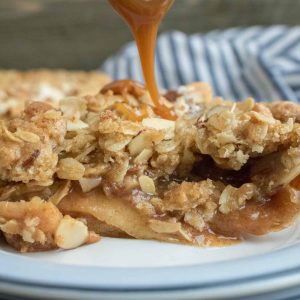 Caramel sauce being drizzled onto a slice of Caramel Apple Crumble Pie served on a white dessert plate