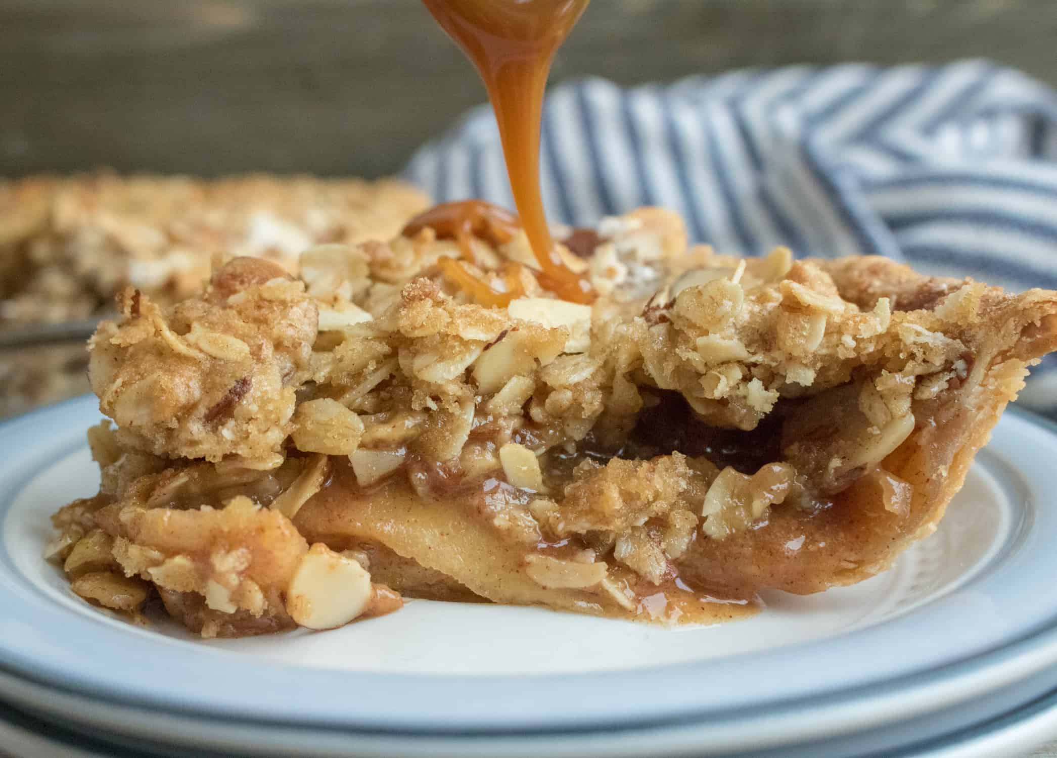 Caramel sauce being drizzled onto a slice of Caramel Apple Crumble Pie served on a white dessert plate 