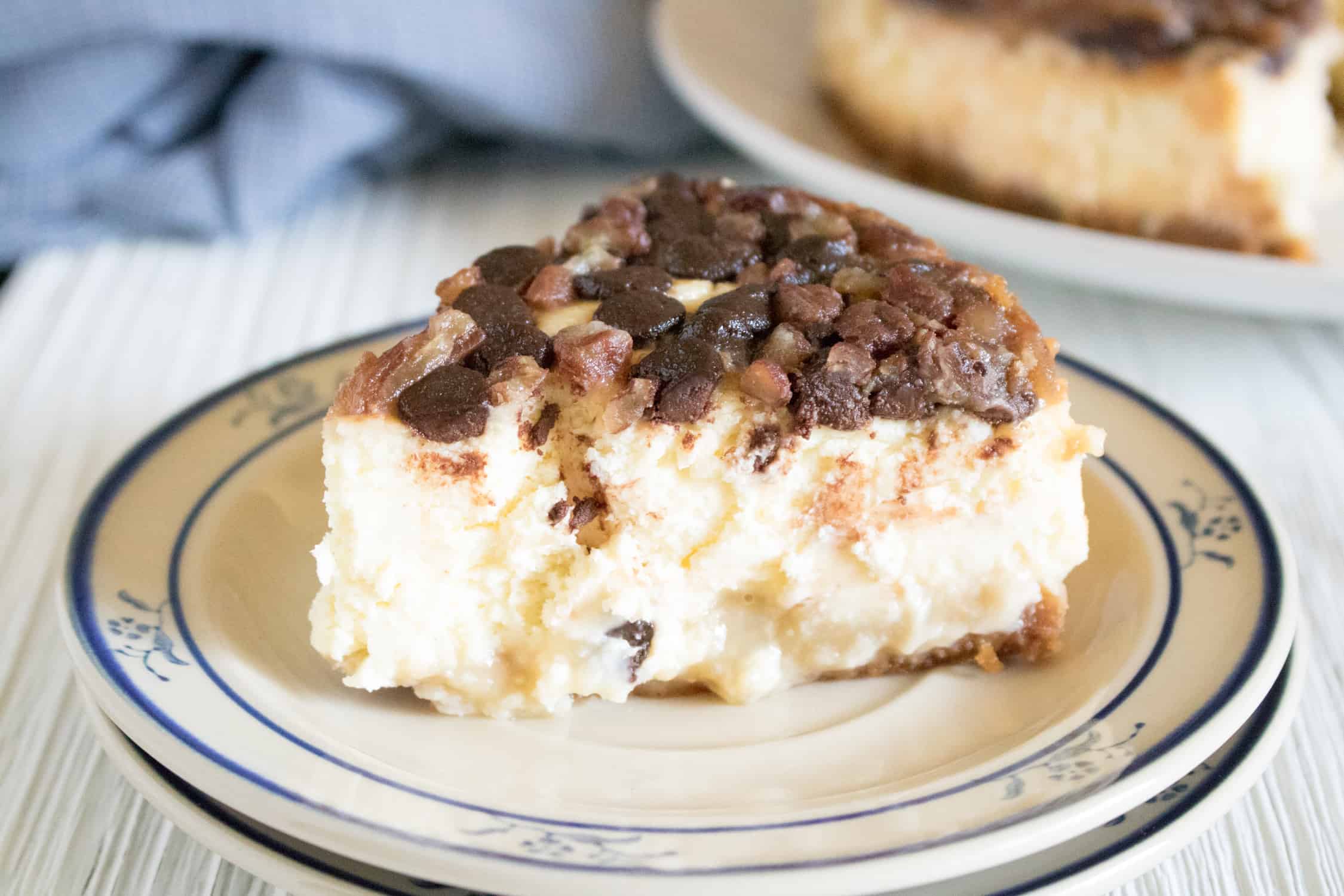 One slice of Instant Pot Pecan Cheesecake with Chocolate Chips on white plate with blue flowers on it